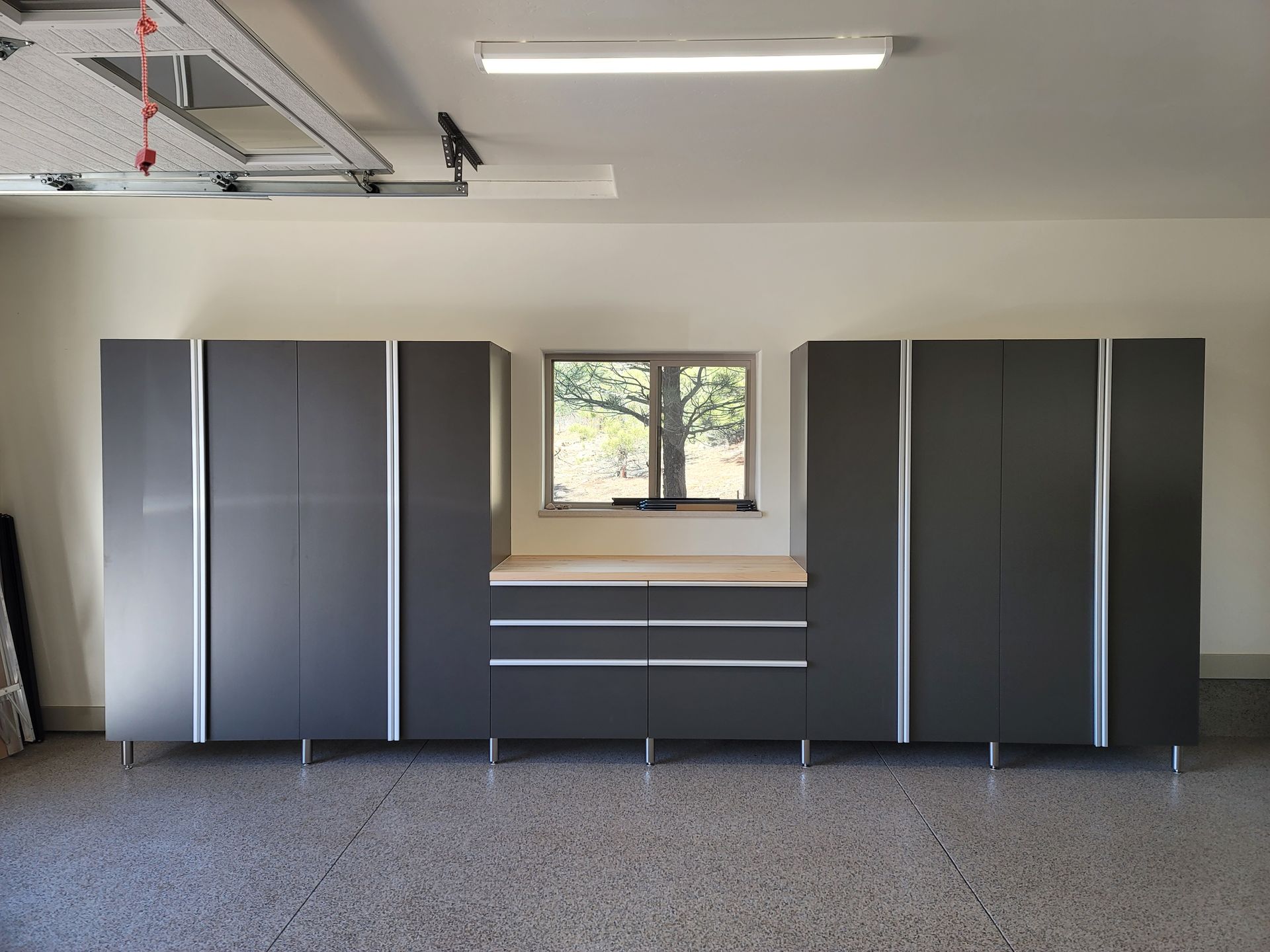 Gray garage cabinets and drawers beneath a small window in a clean workshop space.