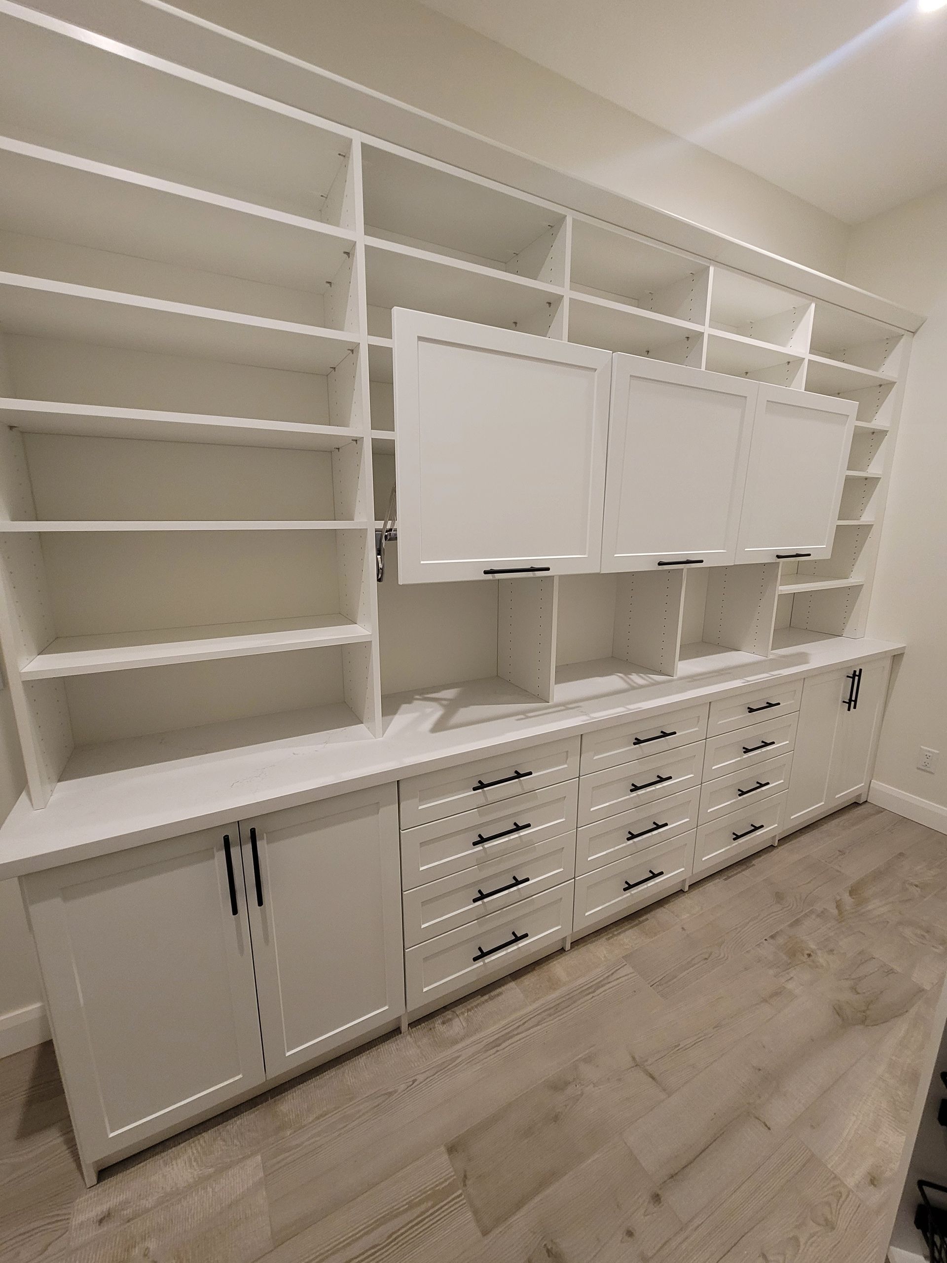 White built-in wall cabinet and shelving unit with drawers in a bright room, viewed at an angle.
