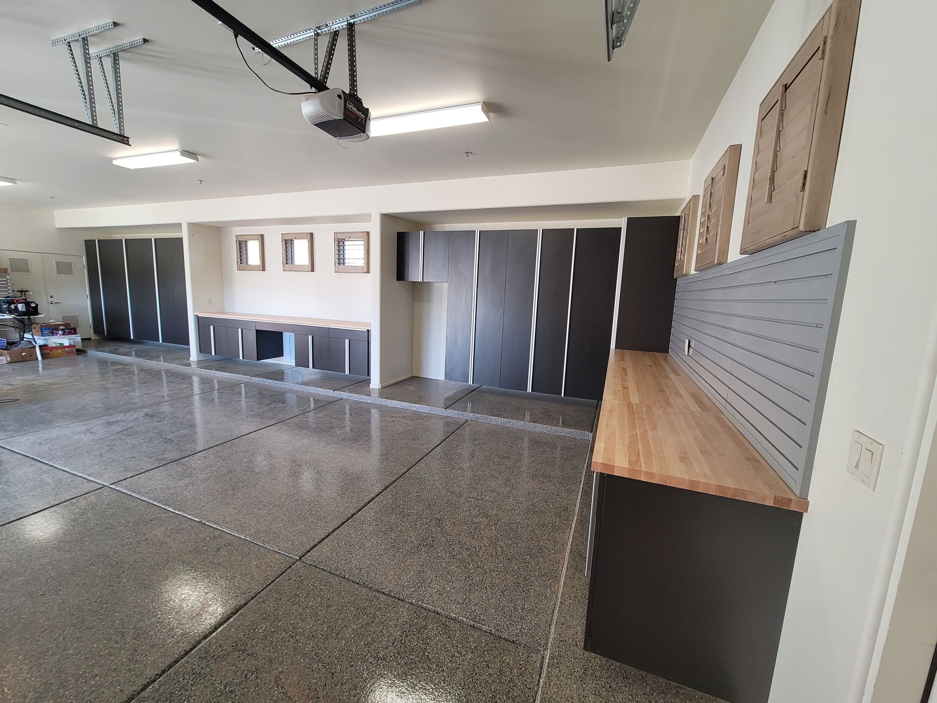 Empty garage interior with polished concrete floor, overhead storage shelves, and closed dark cabinets along the wall