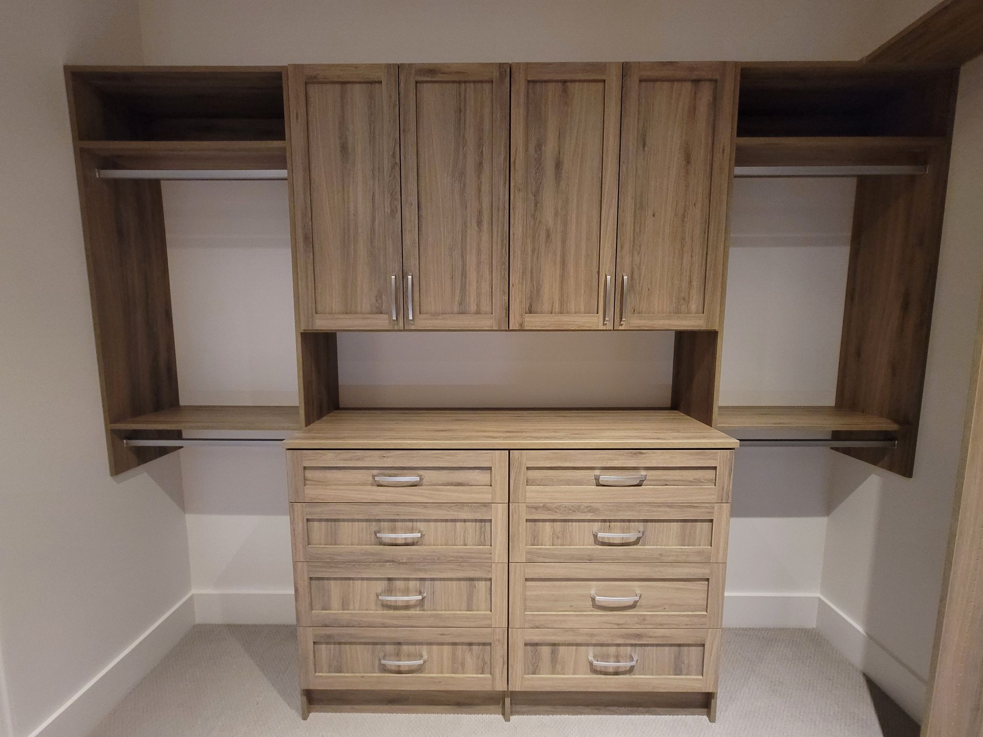 Built-in wood closet and dresser cabinets in a small room with white walls and gray carpet