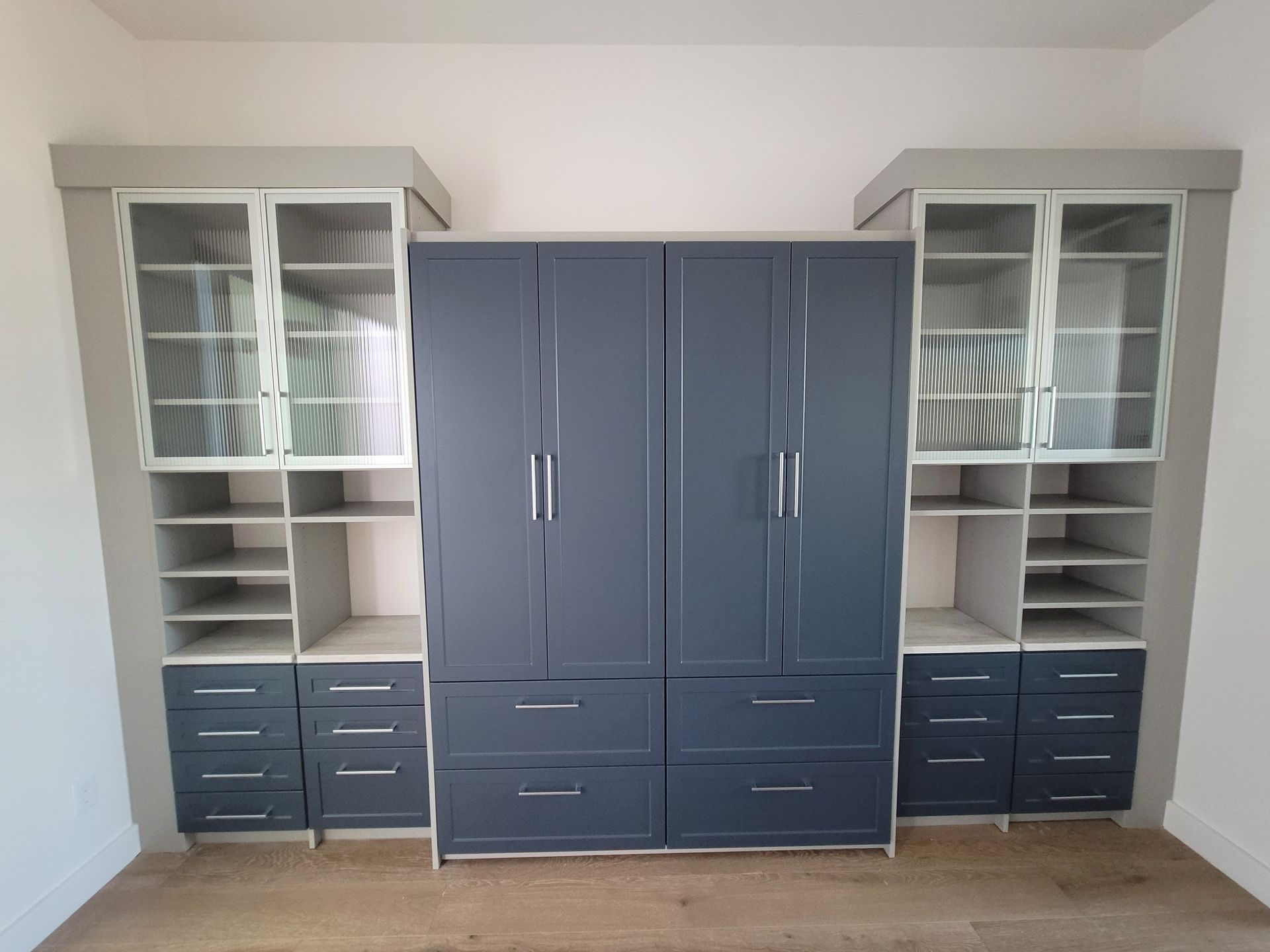 Built-in storage cabinets with glass doors, shelves, and dark gray drawers against a white wall.
