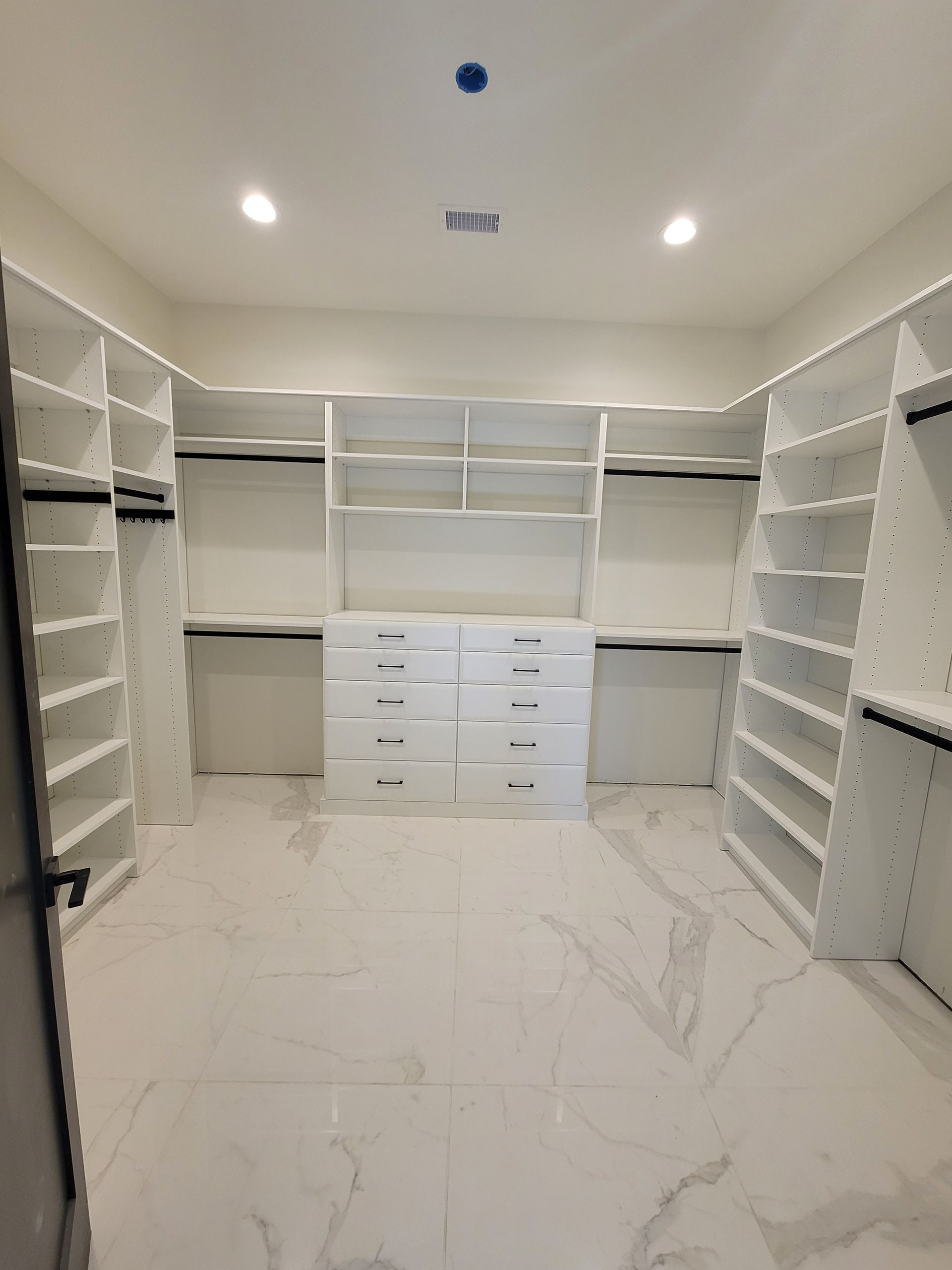 Empty white walk-in closet with built-in shelving, drawers, and glossy marble-look floor