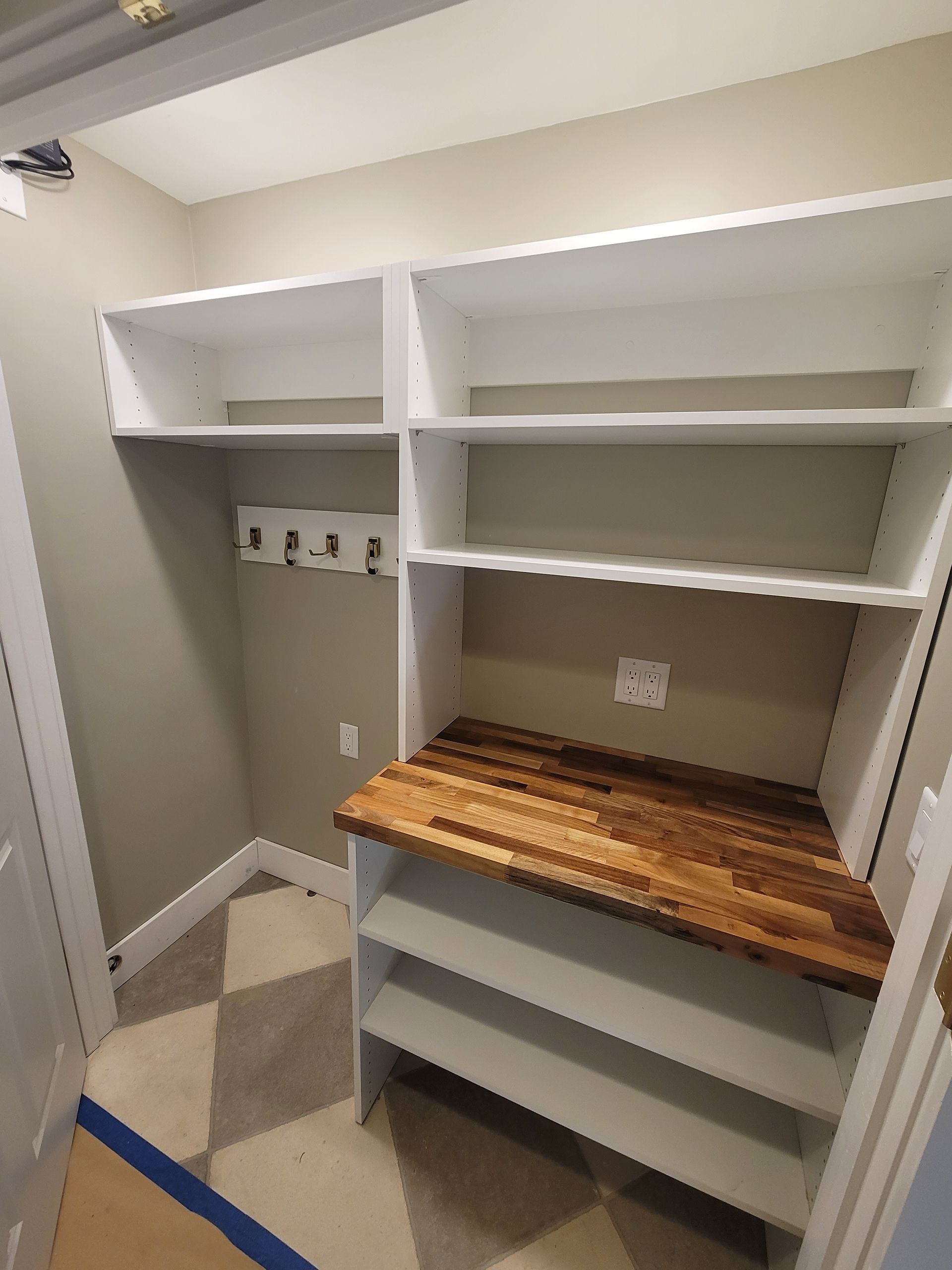 Empty closet with white built-in shelves and a wooden countertop, gray walls, and a checkered floor.