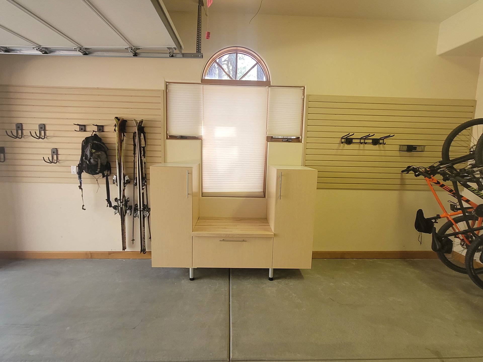 Garage workspace with a beige upholstered chair centered between wall-mounted gear and bicycles.