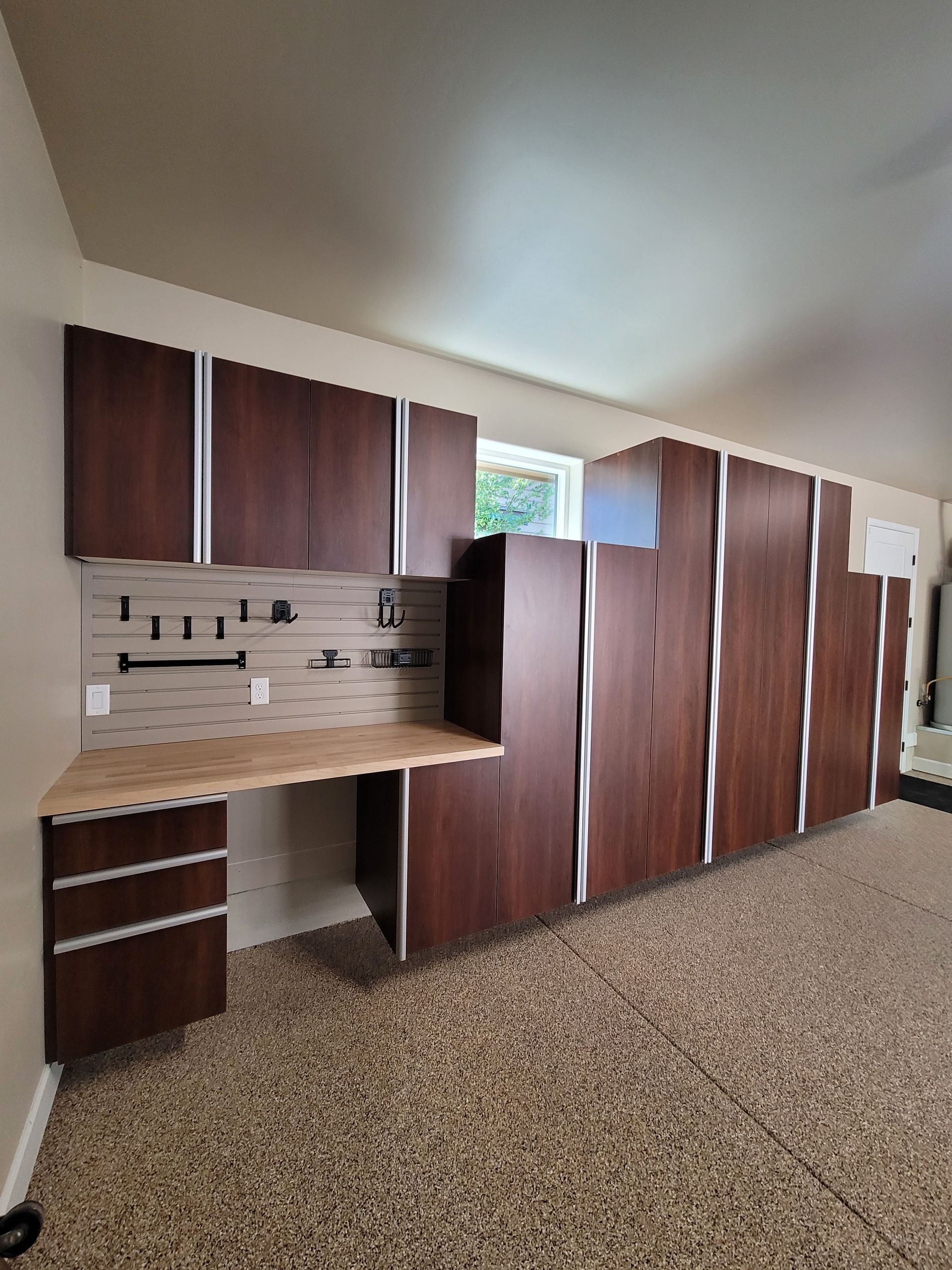 Empty kitchen wall with brown cabinets, beige countertops, and a tiled backsplash on carpeted flooring
