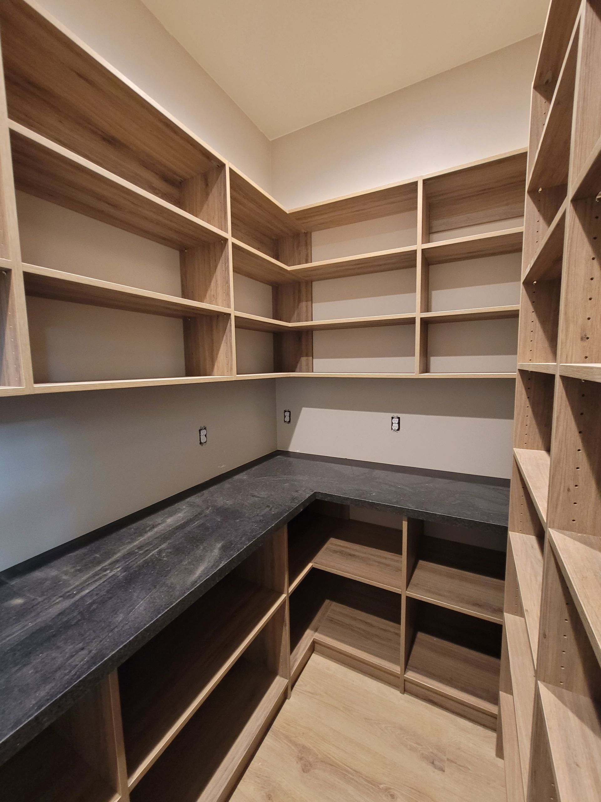 Empty walk-in closet with gray countertops and built-in wooden shelves on three walls.