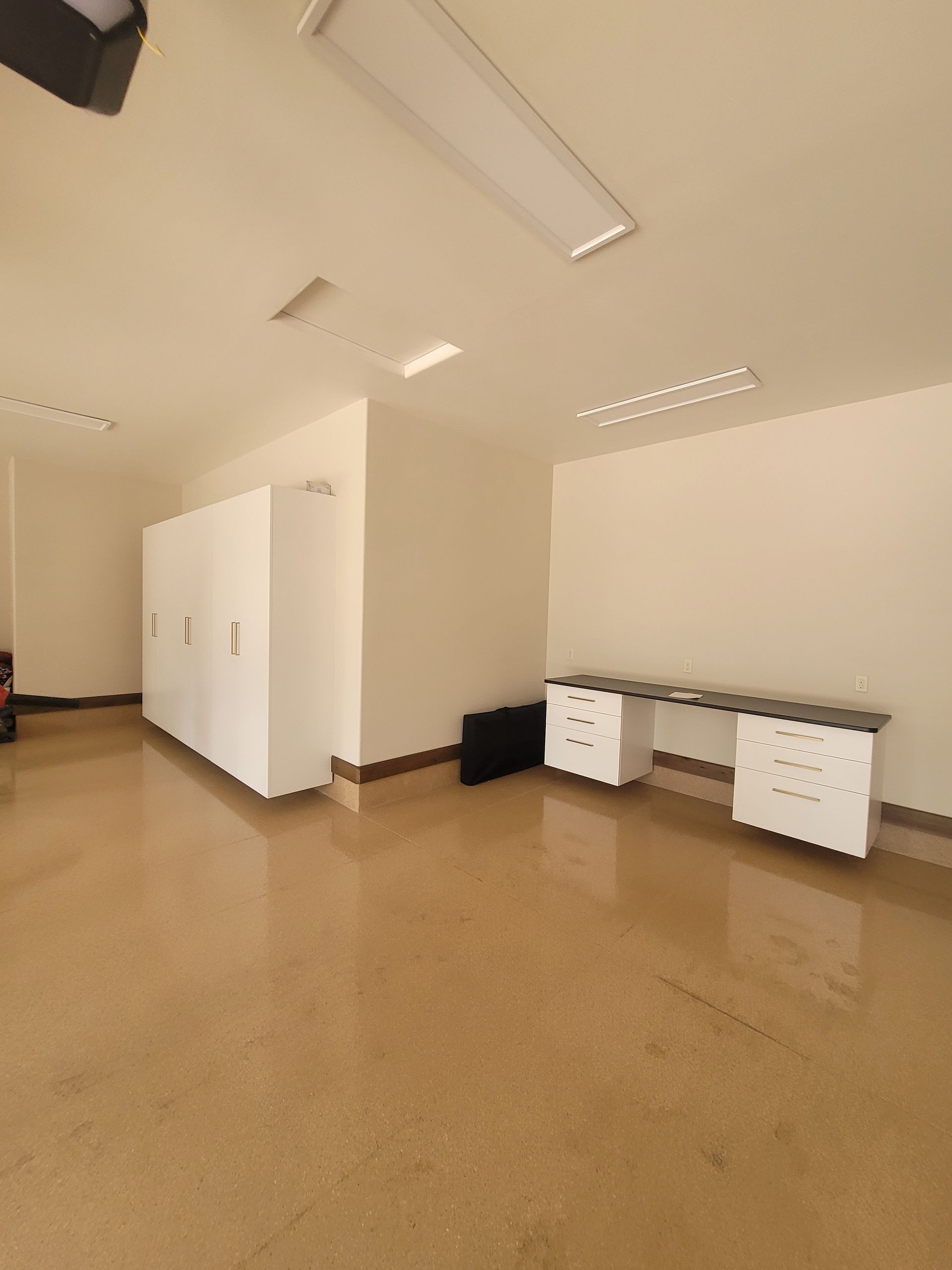 Empty beige room with white cabinets, fluorescent lights, and two small white carts along the wall