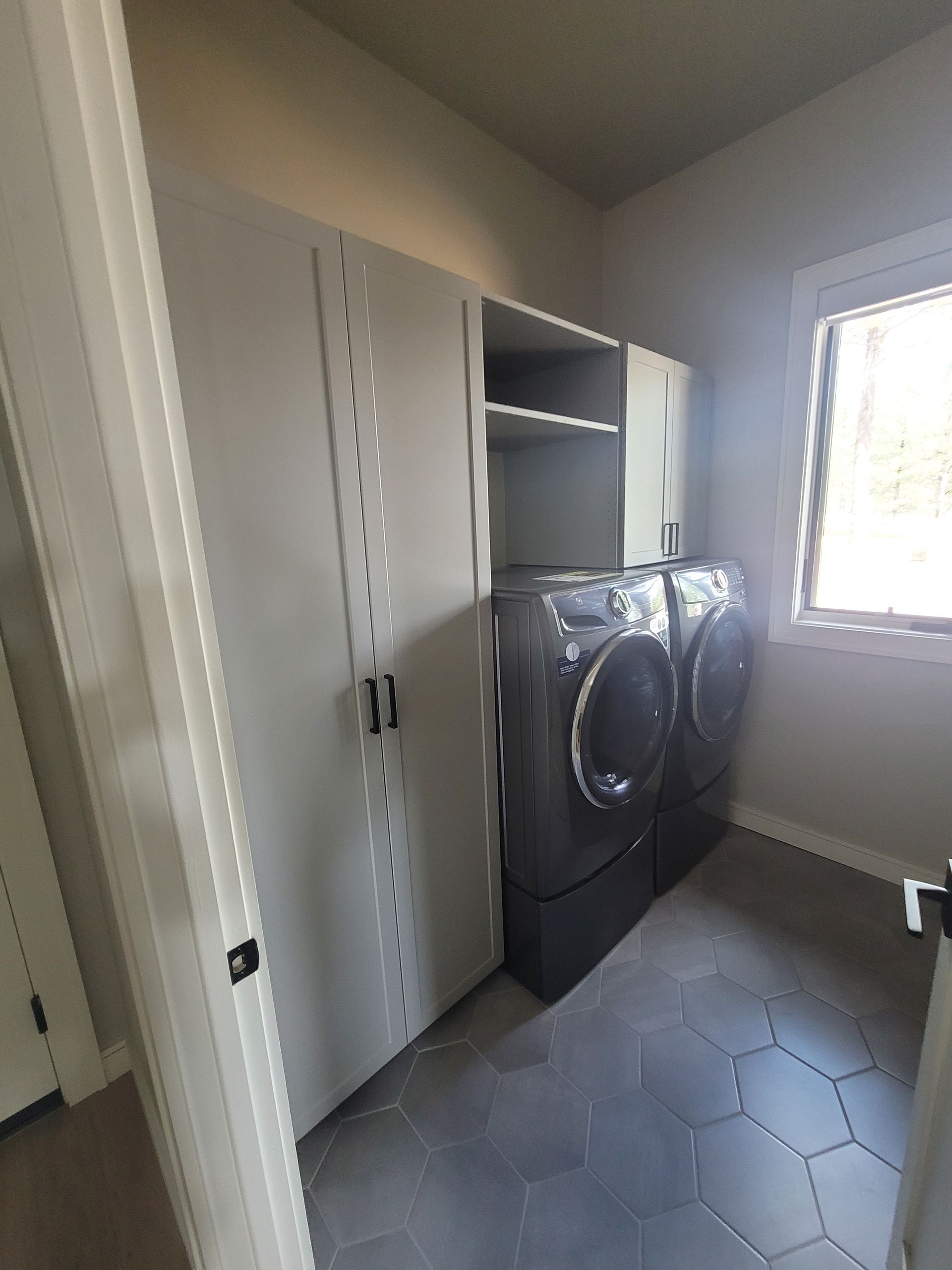 Laundry room with stacked washer and dryer, white cabinets, and a window