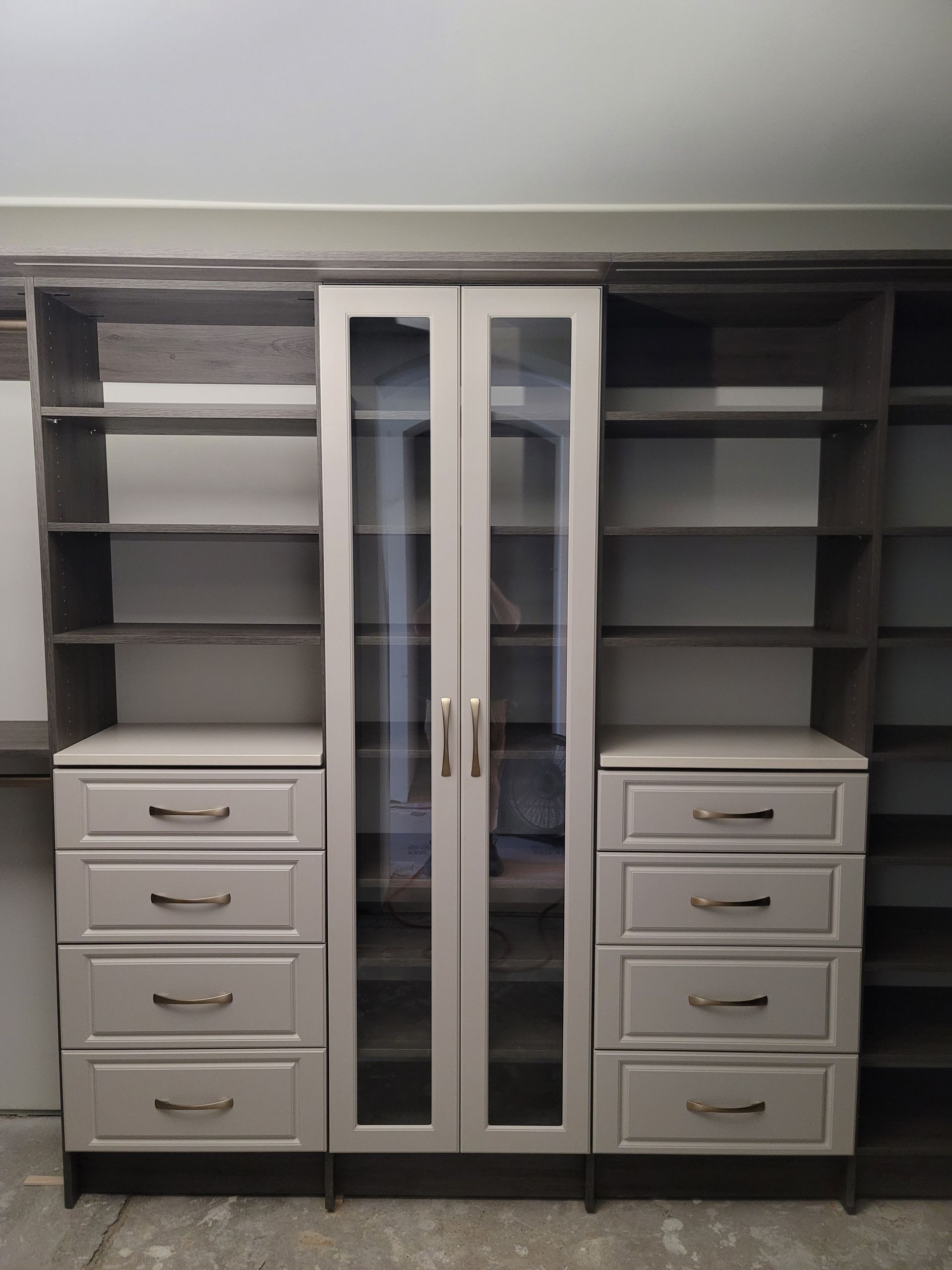 Built-in closet organizers with shelves, drawers, and mirrored center cabinet in a beige room