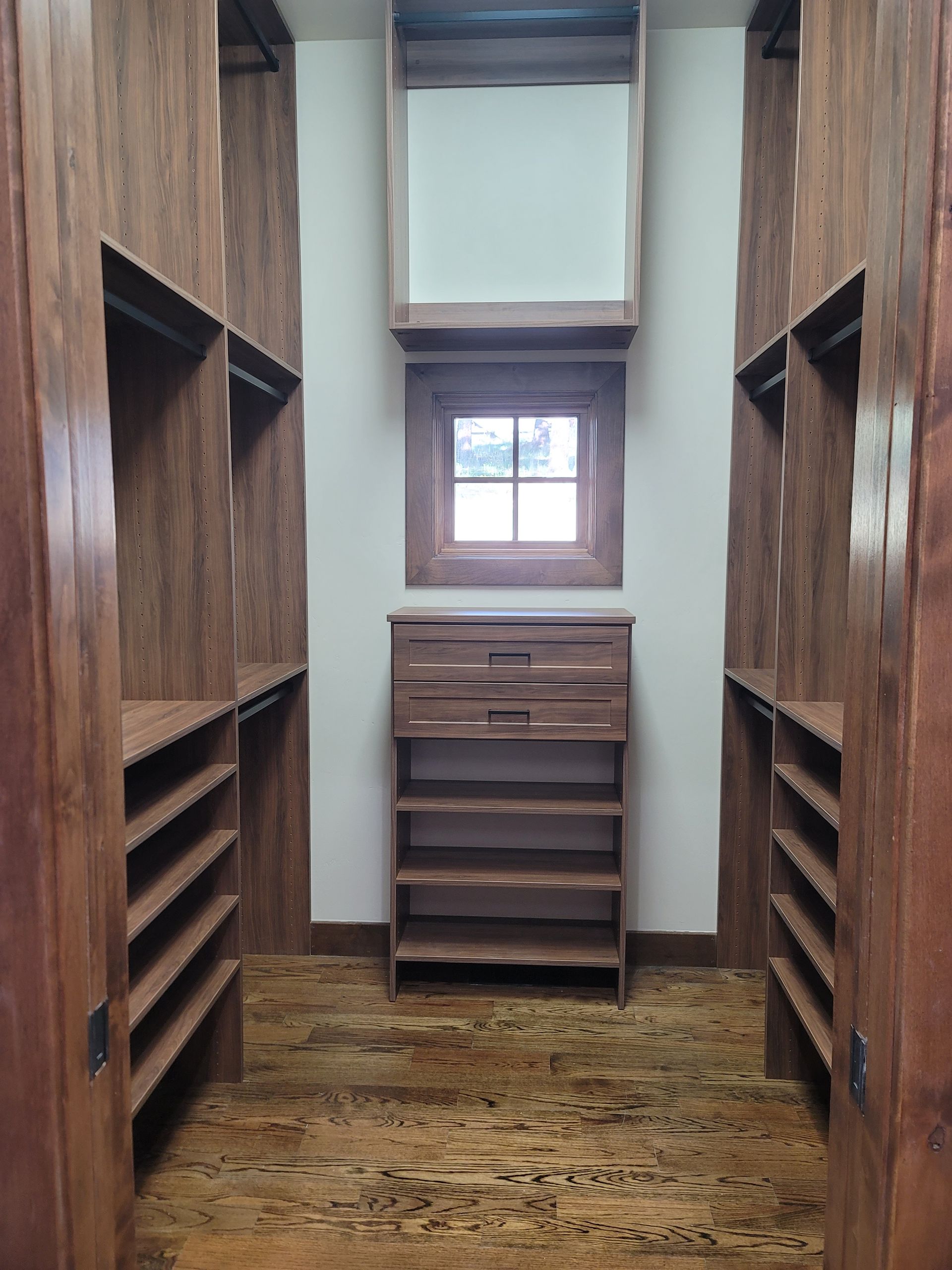 Narrow wooden hallway with built-in shelves, a small cabinet, and a window at the far end.