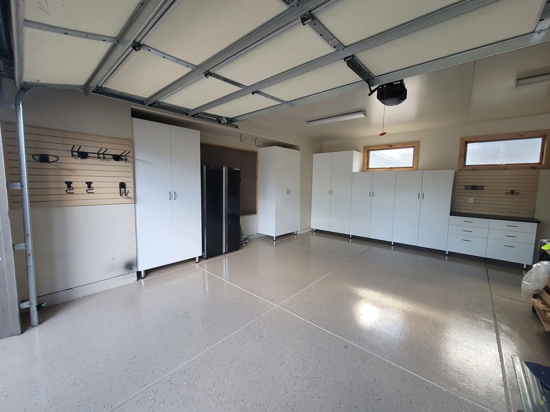 Empty garage interior with white cabinets, epoxy floor, and overhead storage racks