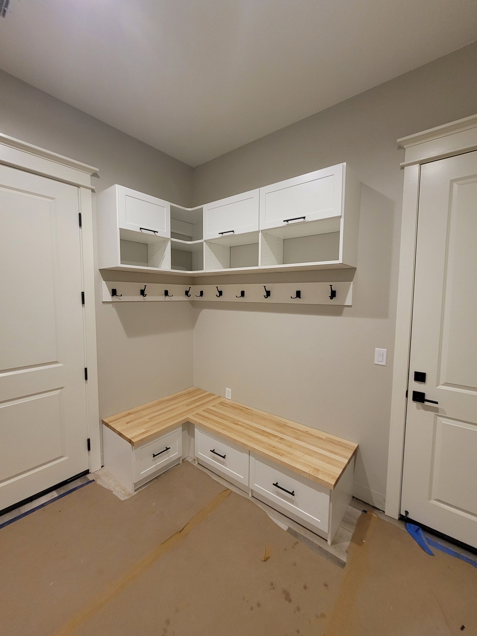 Small mudroom with white built-in cubbies, hooks, and a bench against beige walls and carpet.