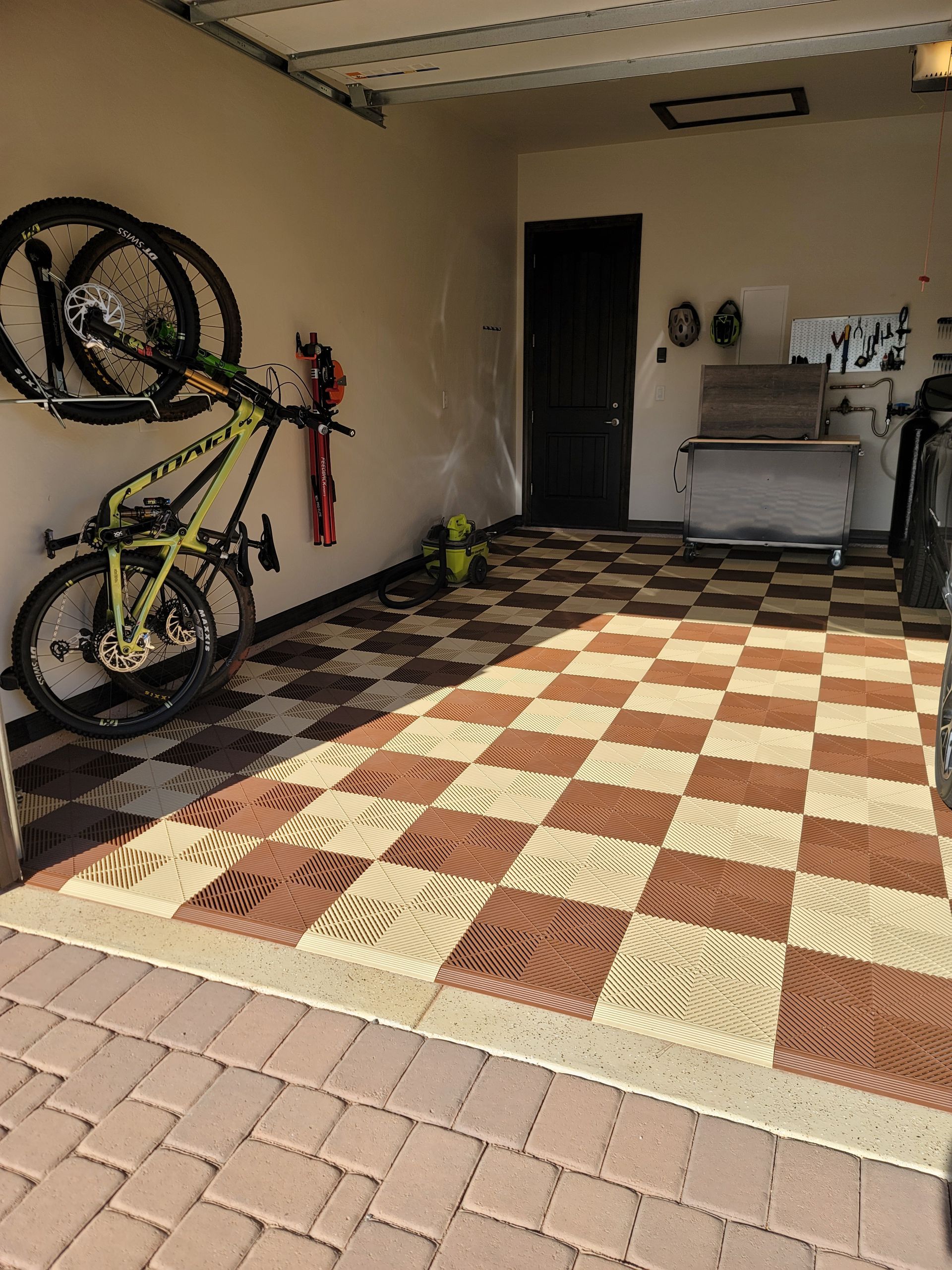 Garage with two bicycles on the left, checkered floor mat, and storage shelves in the back.
