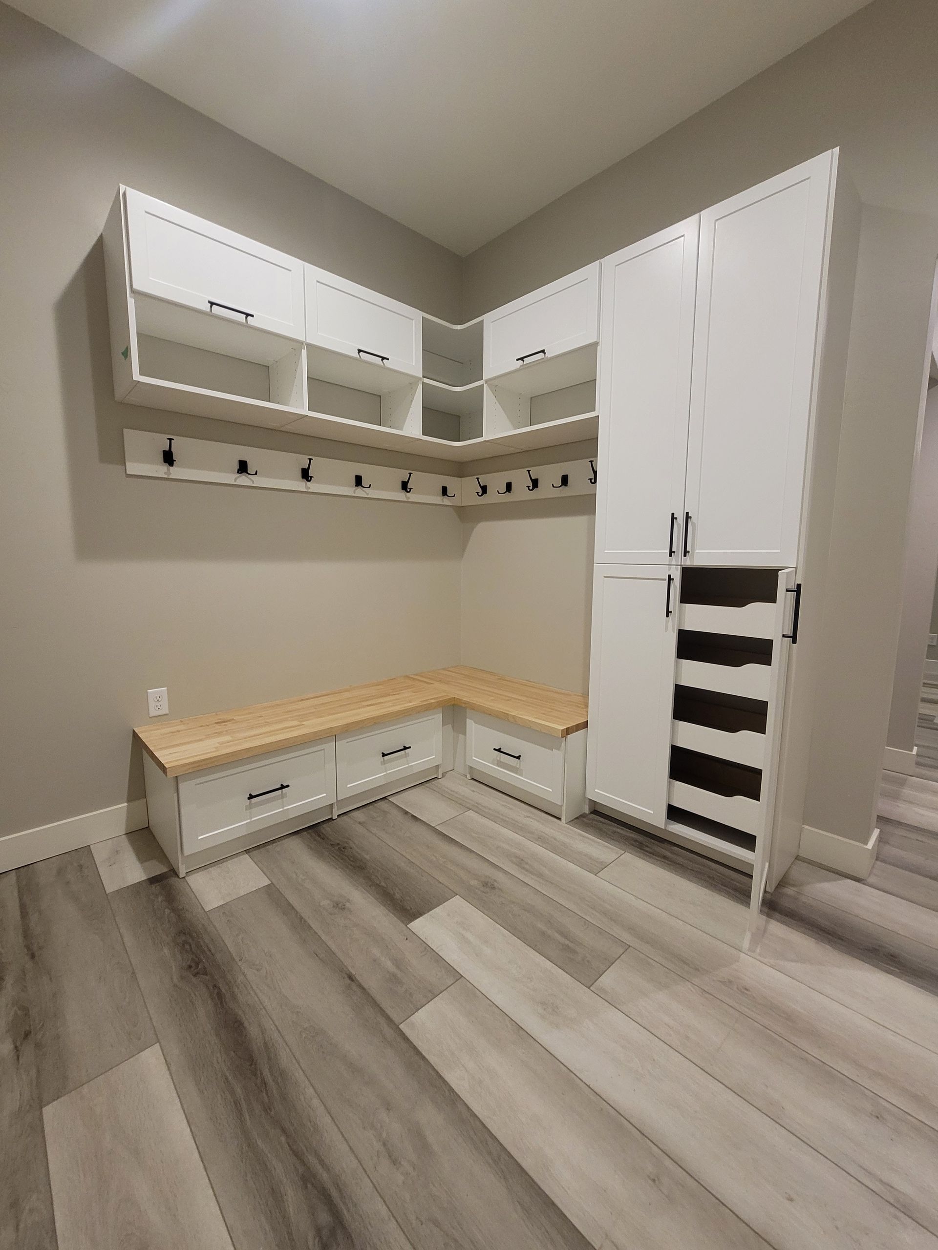 Bright walk-in closet with white cabinets, wood bench, and hanging storage shelves