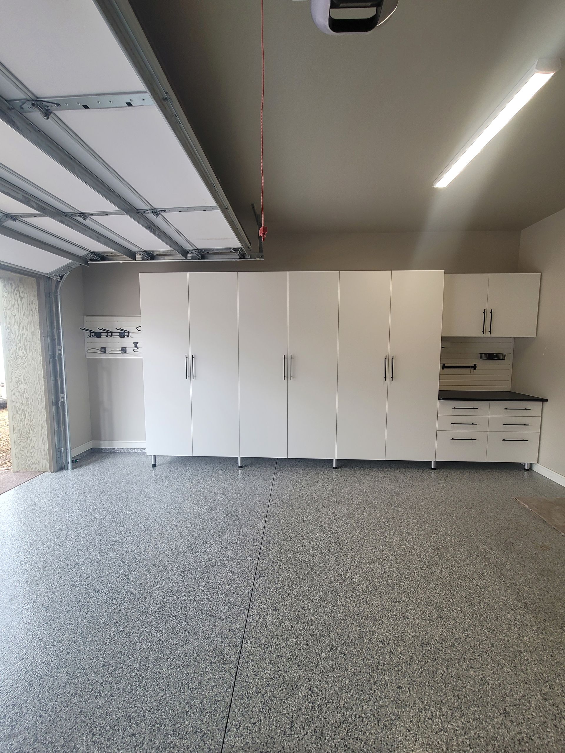 Empty modern garage with white cabinets and speckled gray floor, lit by overhead lights