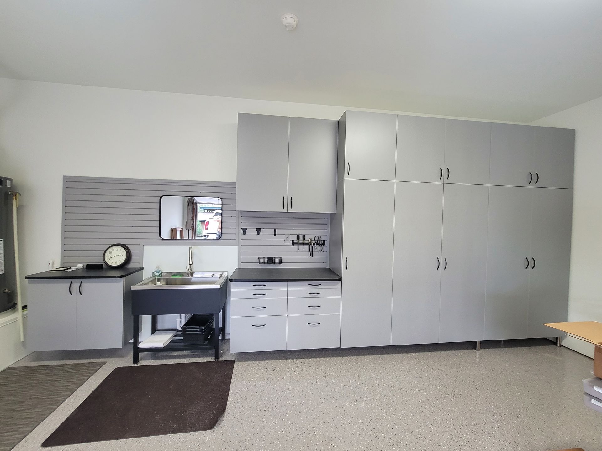 Clinic room with sink, desk, cabinets, and a large storage wall in a bright, sparse space