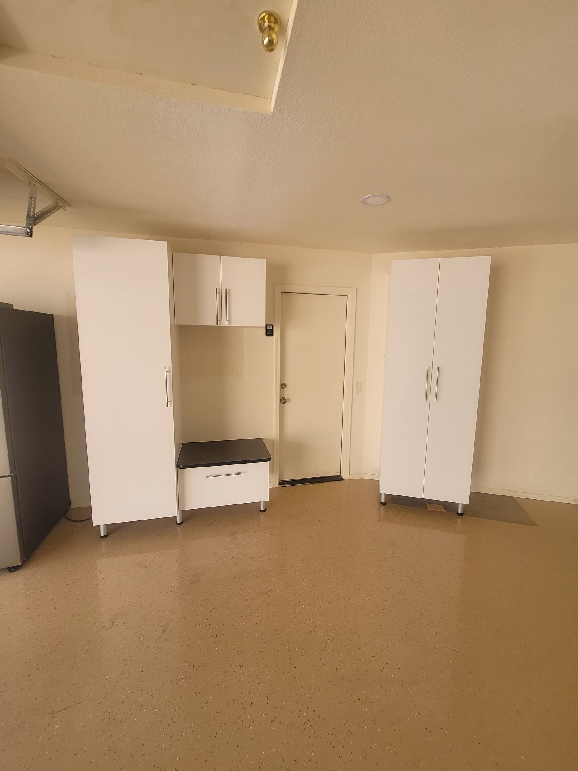 Small empty room with white cabinets, a door, and a beige floor.