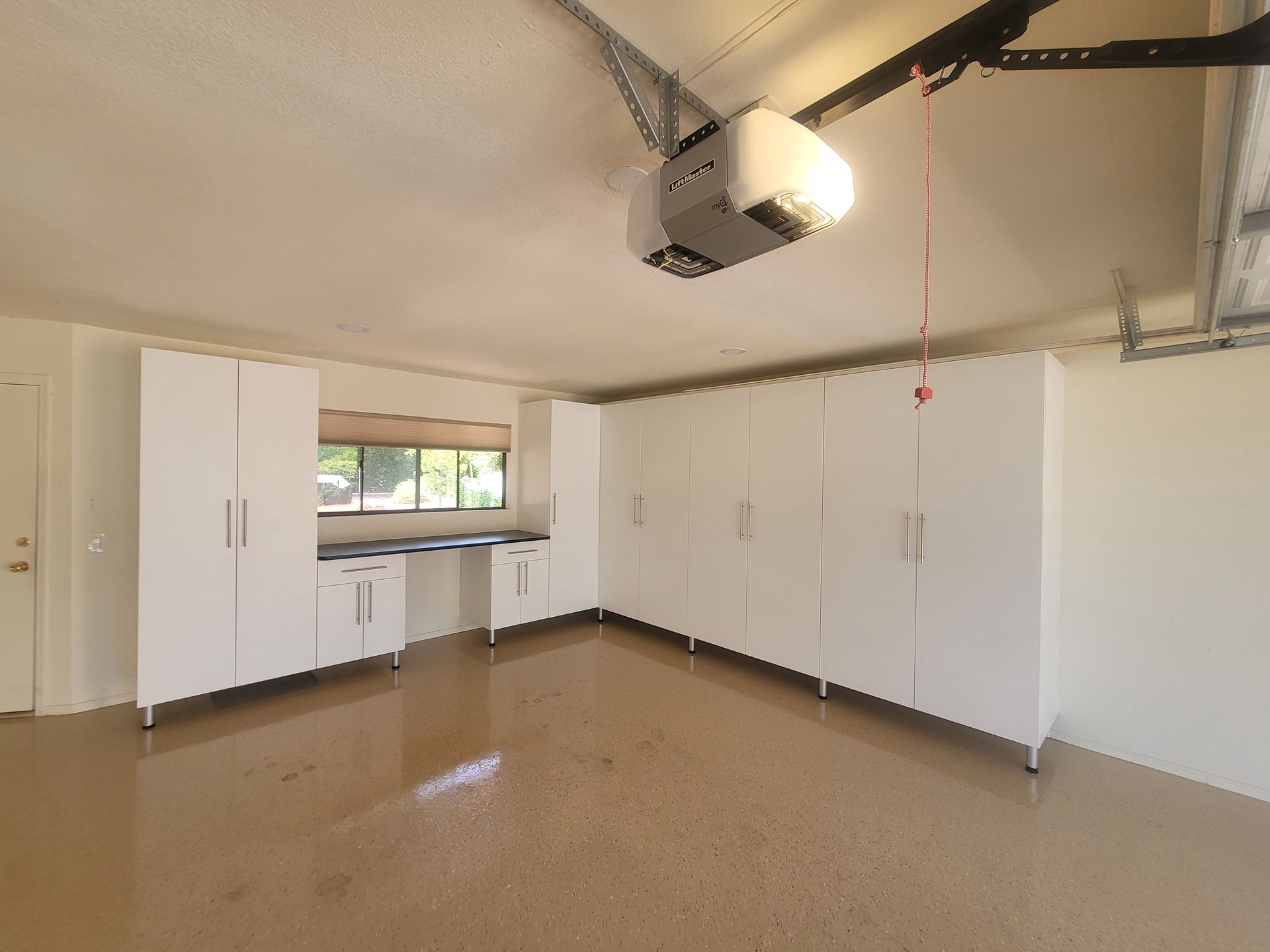 Empty garage with white cabinets, window, and overhead garage door opener.