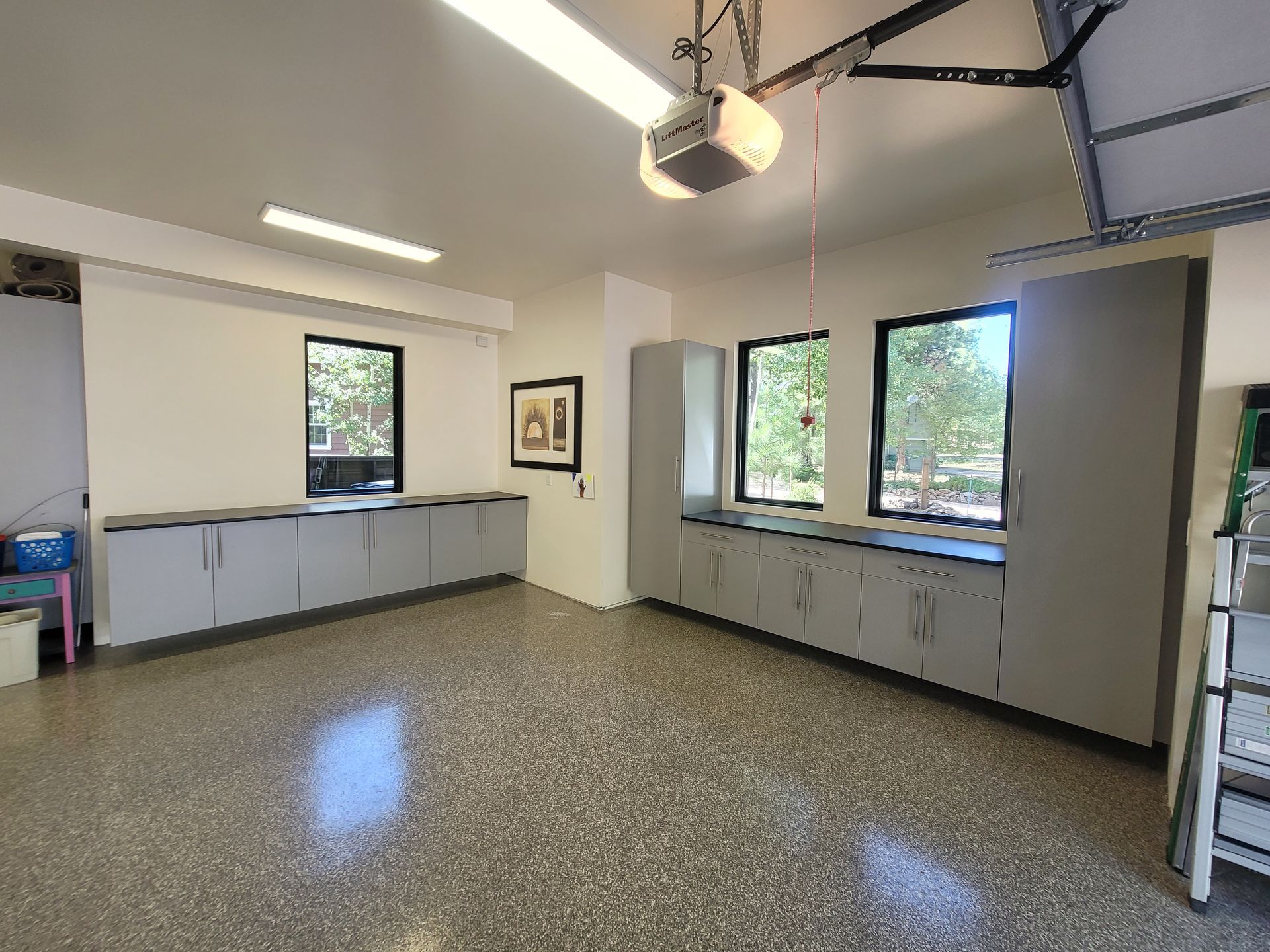 Empty garage-like room with cabinets, windows, and overhead lights on a speckled floor.