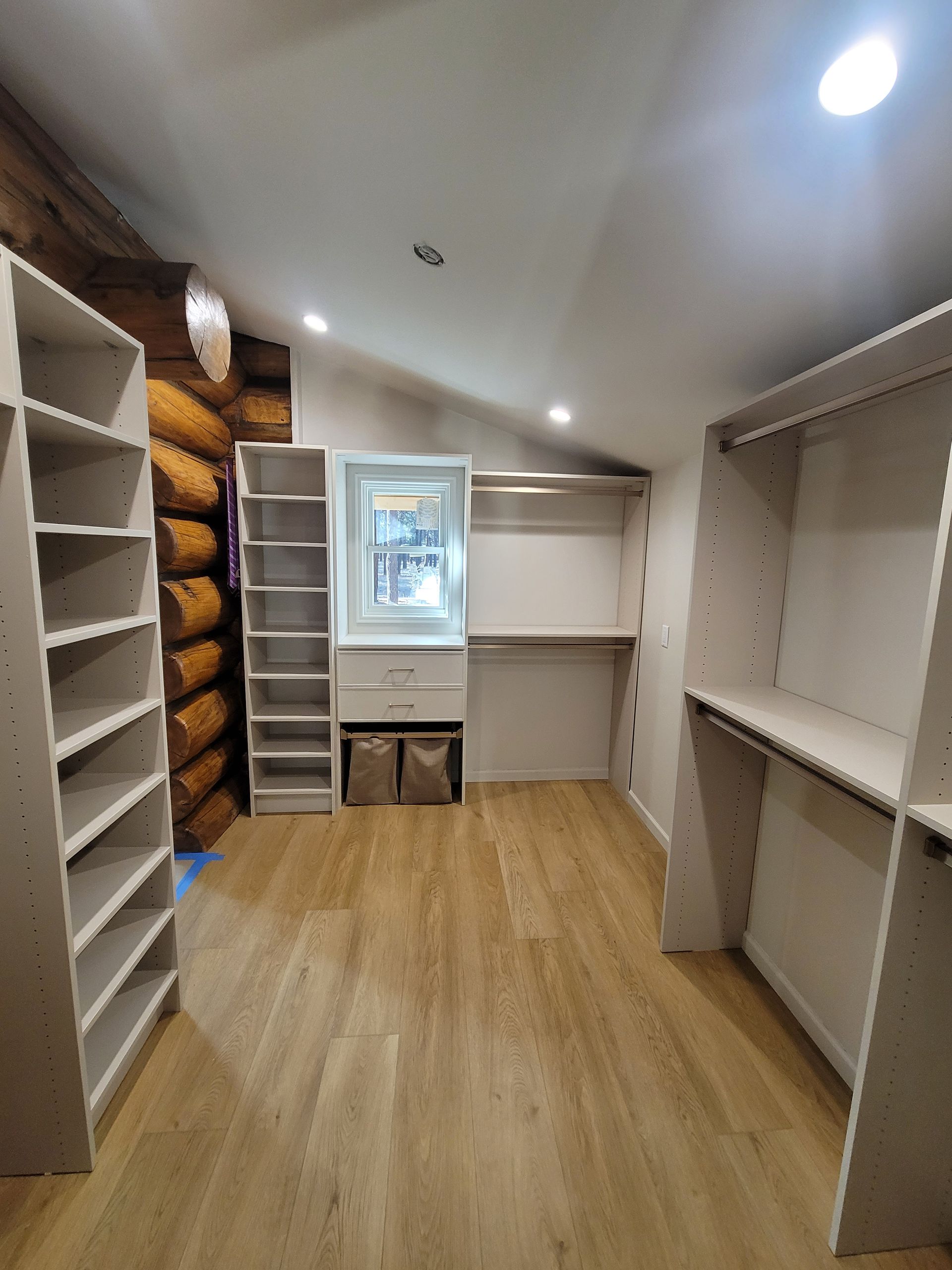 Built-in wood closet wall with drawers, shelves, and two small windows above a hardwood floor