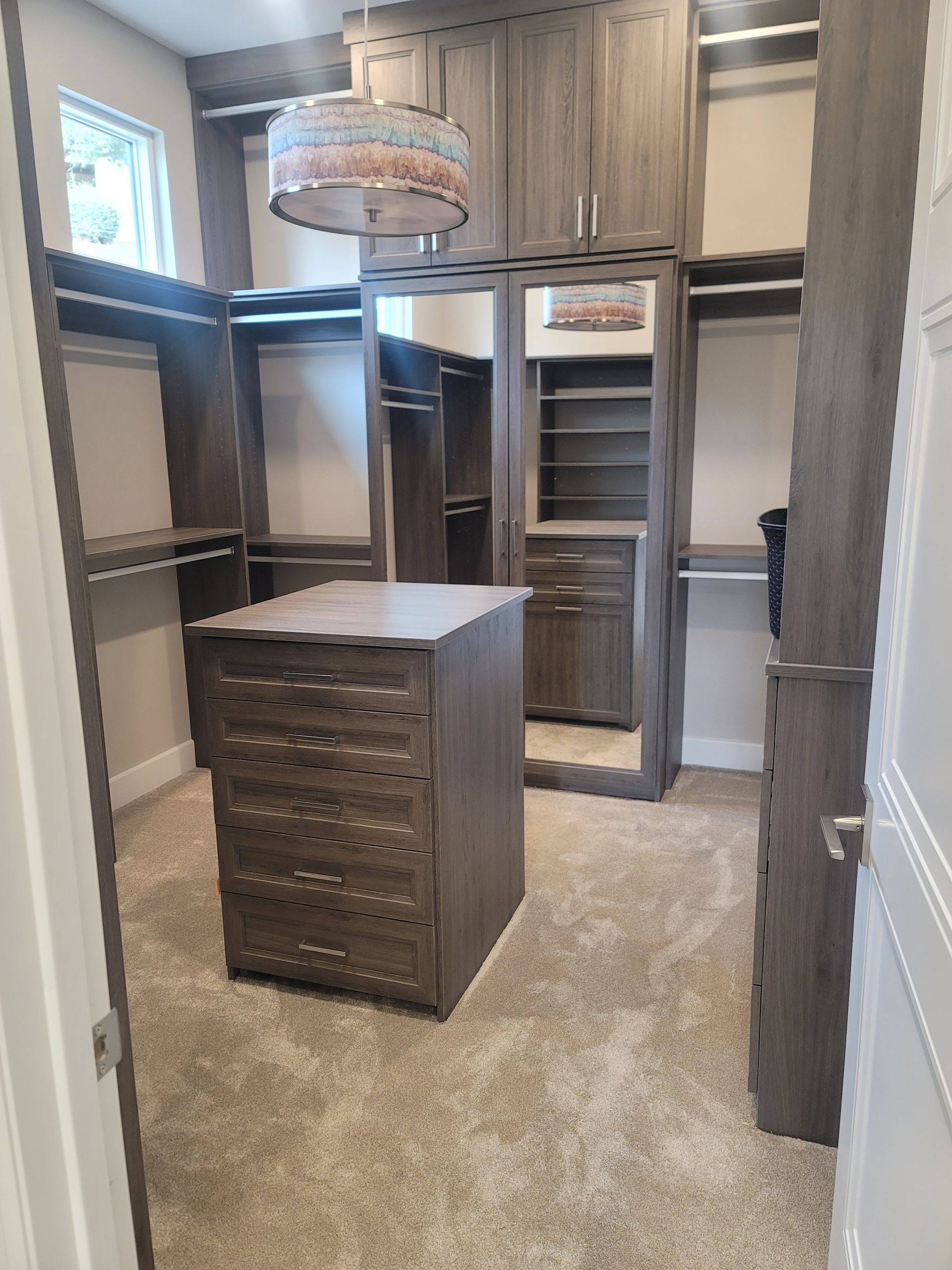 Walk-in closet with built-in shelves, hanging rods, and a central drawer cabinet in beige and wood tones
