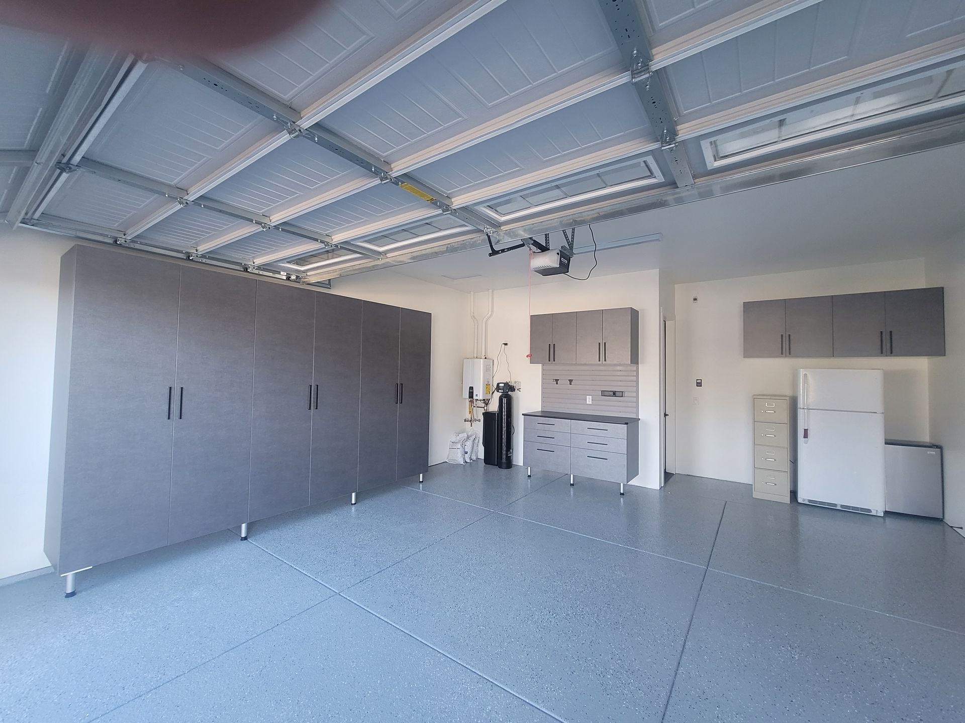 Empty garage with gray cabinets, white appliances, and a speckled floor under a metal ceiling.