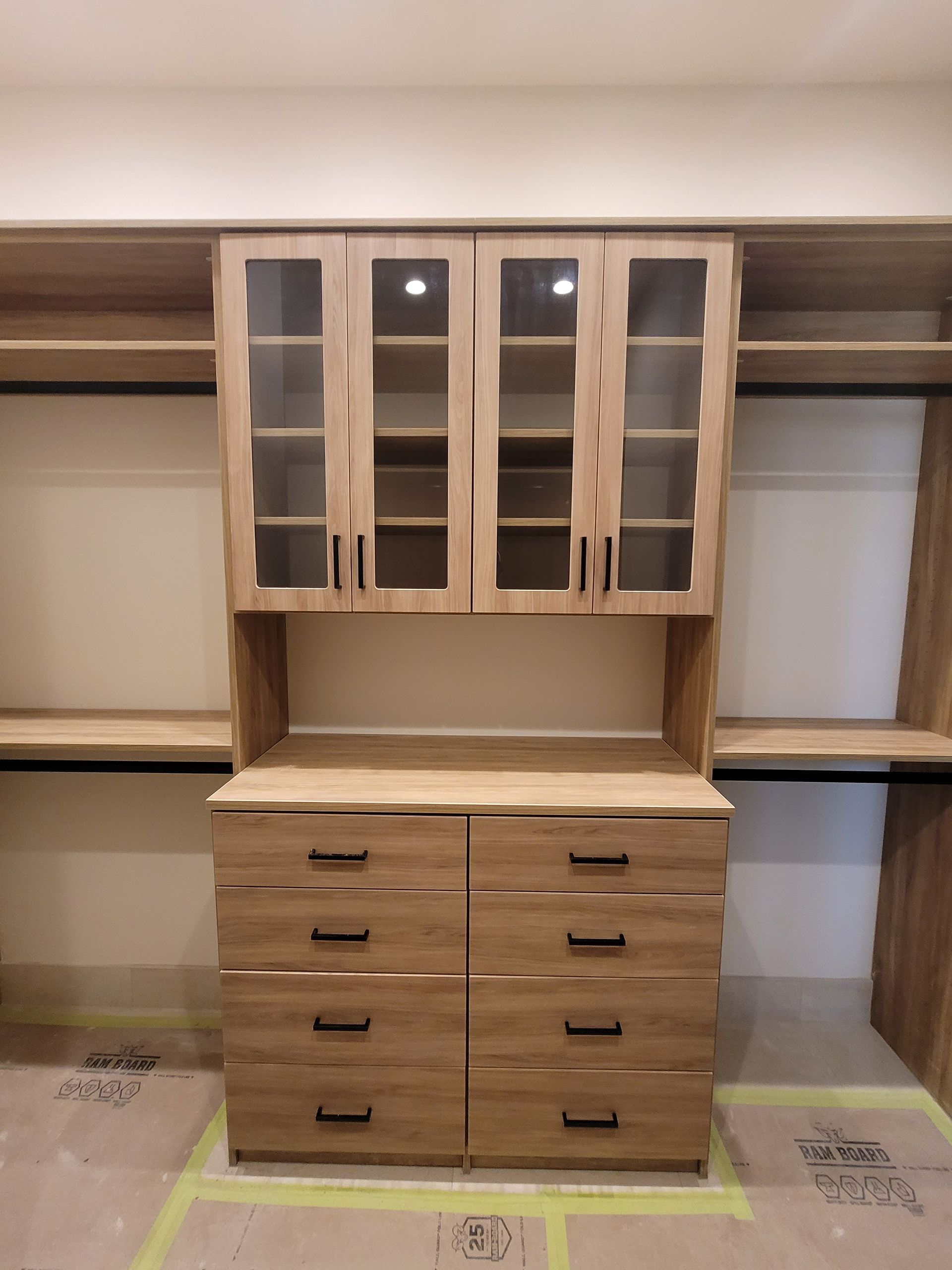 Built-in wooden closet with drawers, open shelves, and glass-front cabinets against a wall.