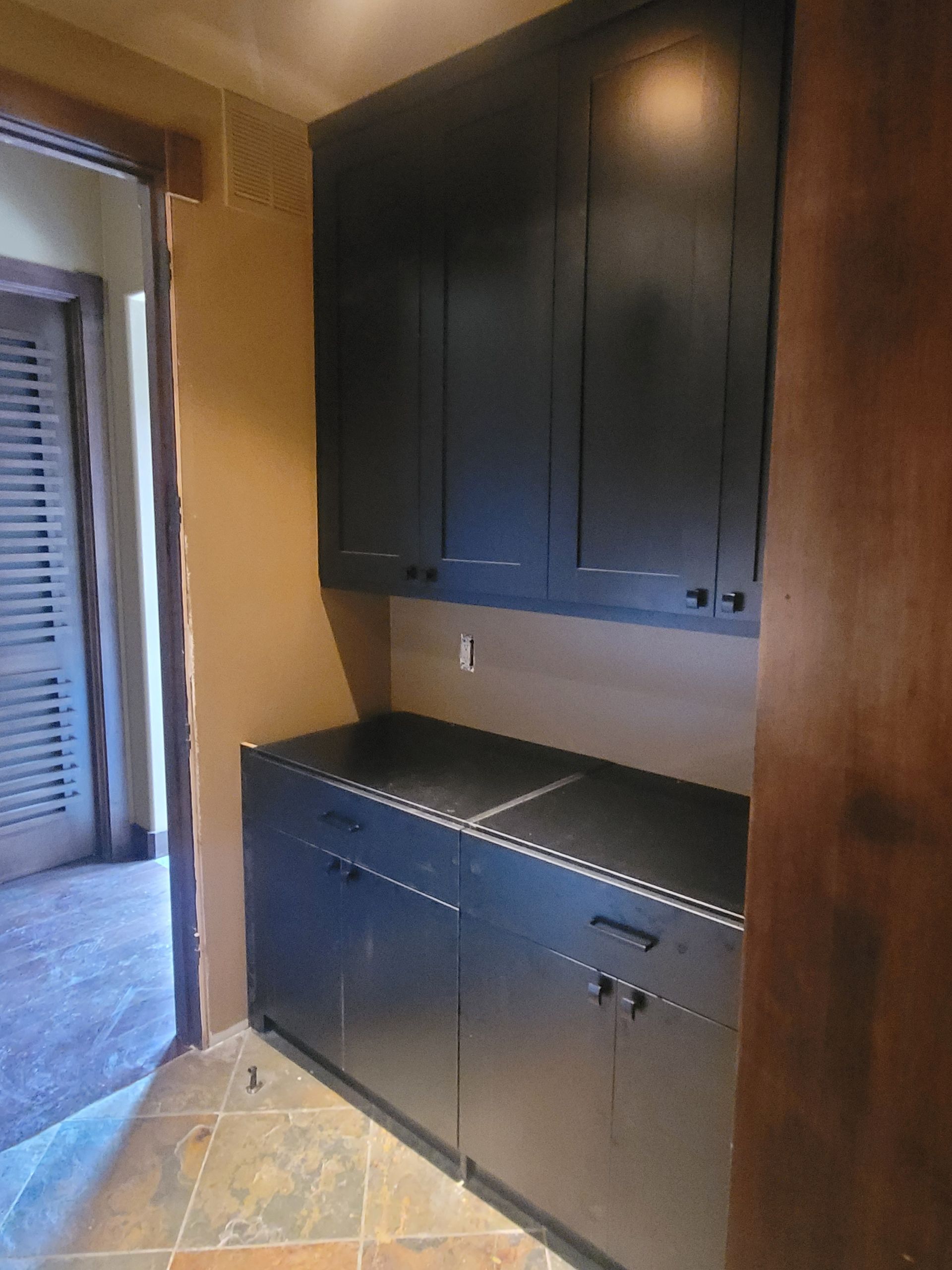 Built-in black cabinets and countertop in a small entry alcove beside a doorway.