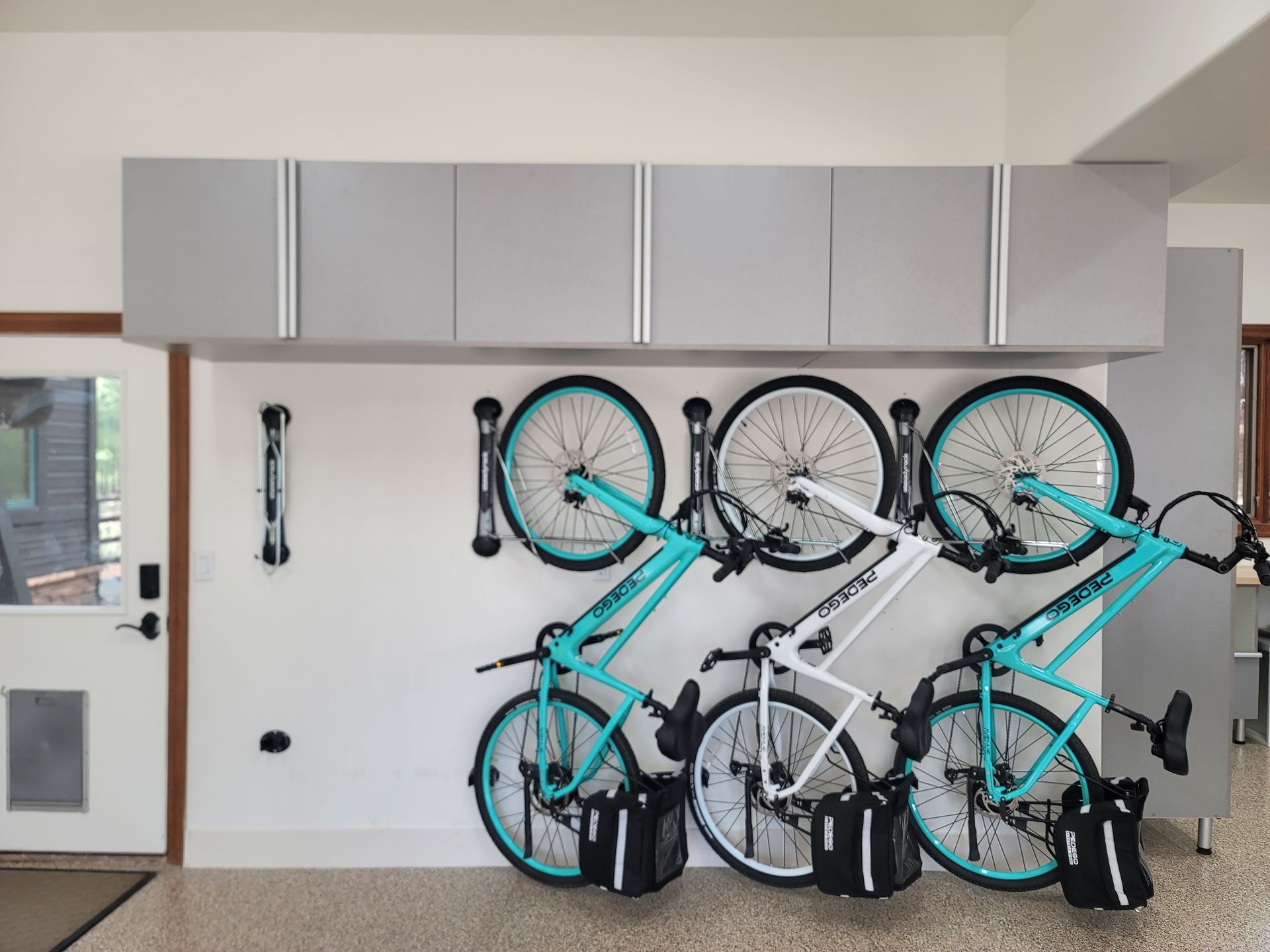 Several bicycles stacked and hanging on a white wall beneath gray cabinets in a garage