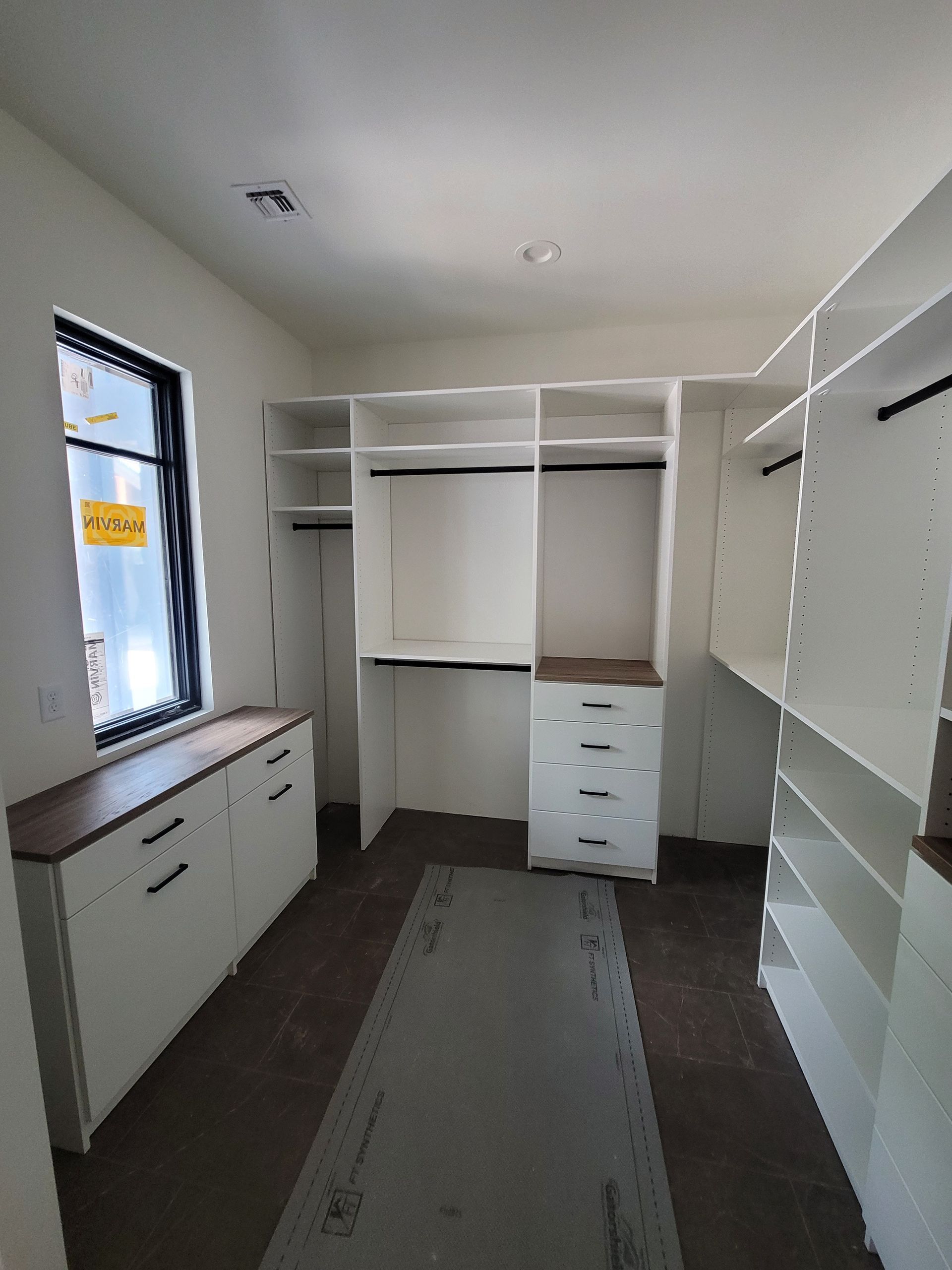 Empty walk-in closet with white shelves, drawers, and a window on the left.