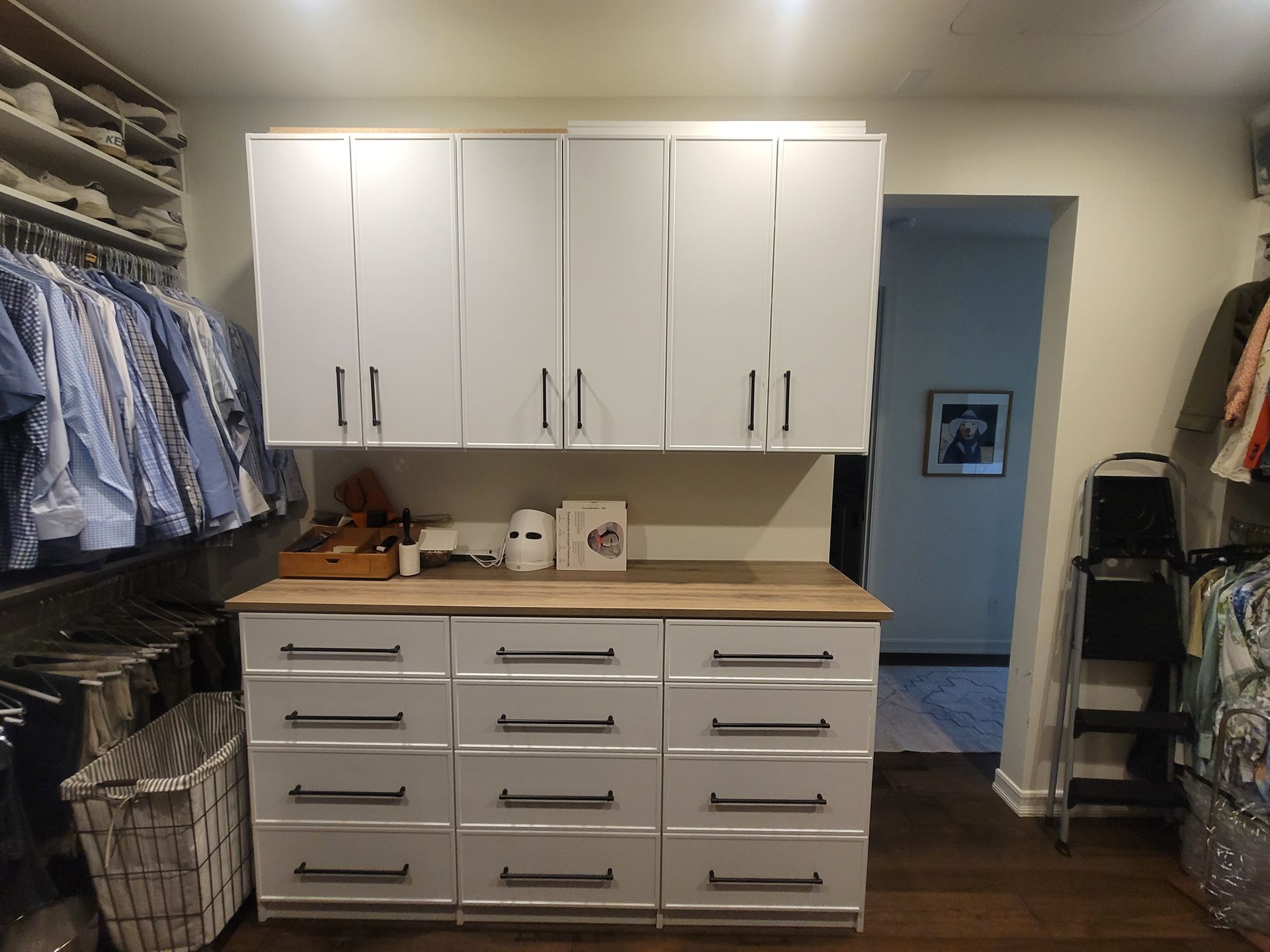 White cabinets and drawers in a walk-in closet with hanging clothes and storage bins on both sides