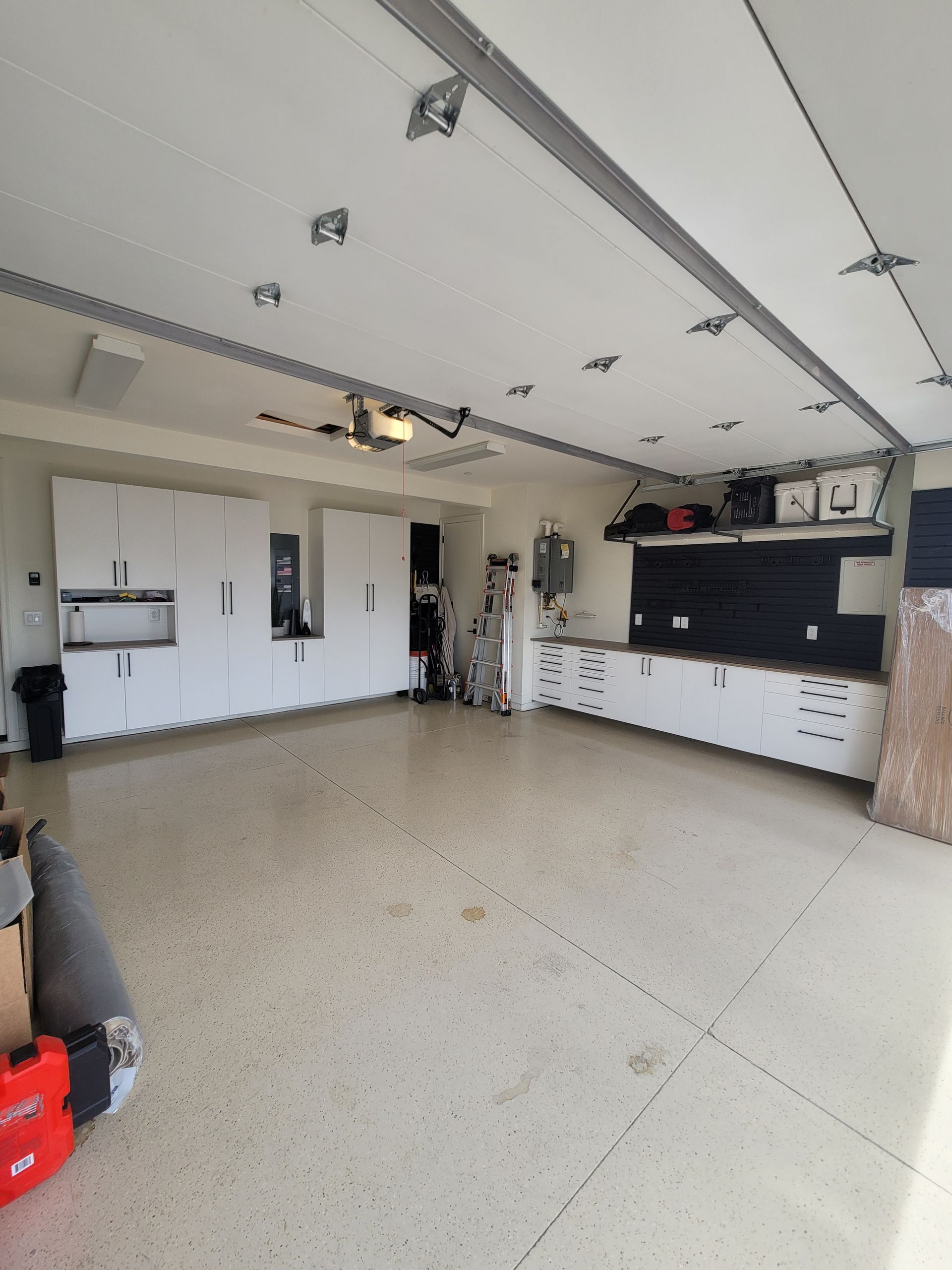 Spacious white garage with closed door, wall cabinets, and a workbench area with tools and storage shelves.