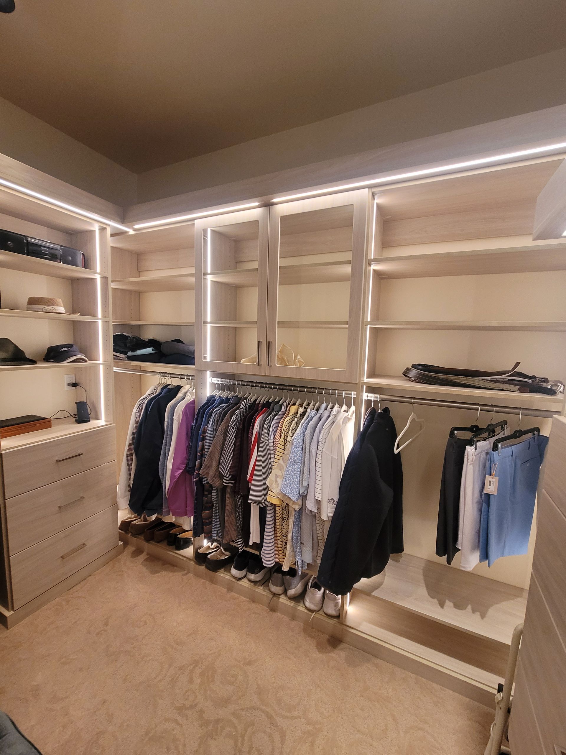 Walk-in closet with white shelving, hanging clothes, and beige carpet.