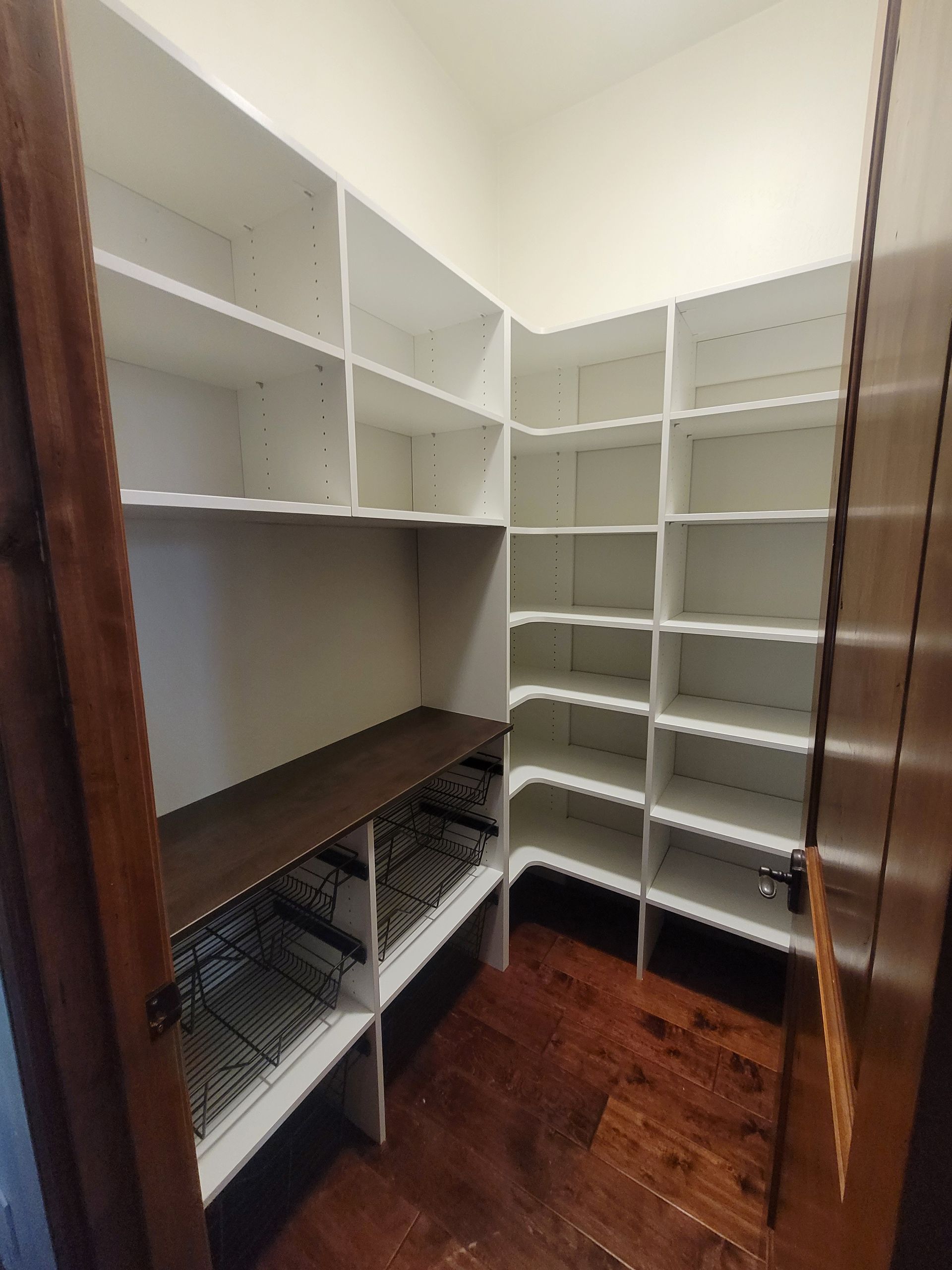 Walk-in closet with white shelves, hanging rods, wire baskets, and dark wood flooring