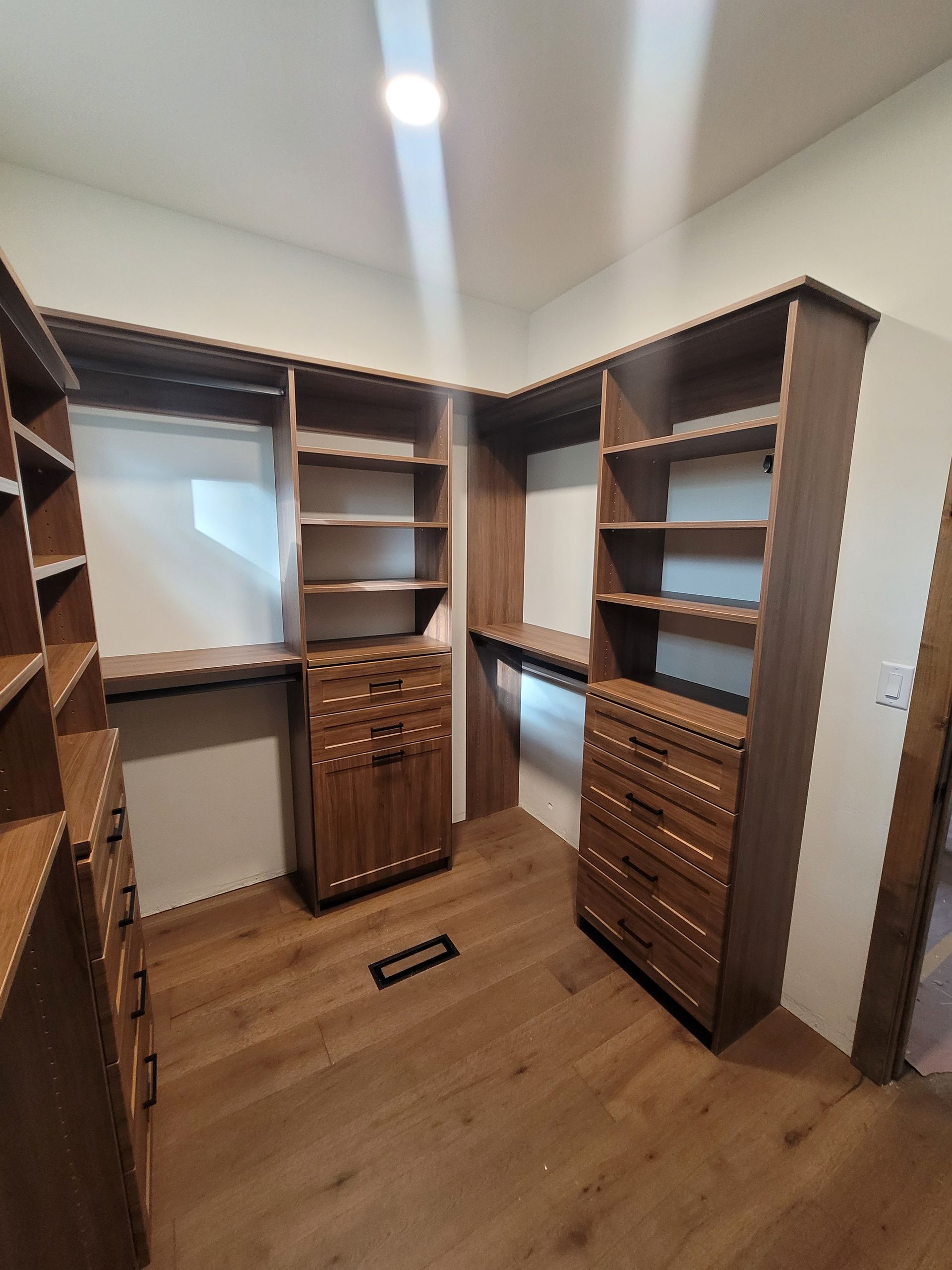 Walk-in closet with dark wood shelving, drawers, hanging rods, and a ceiling light on wood flooring