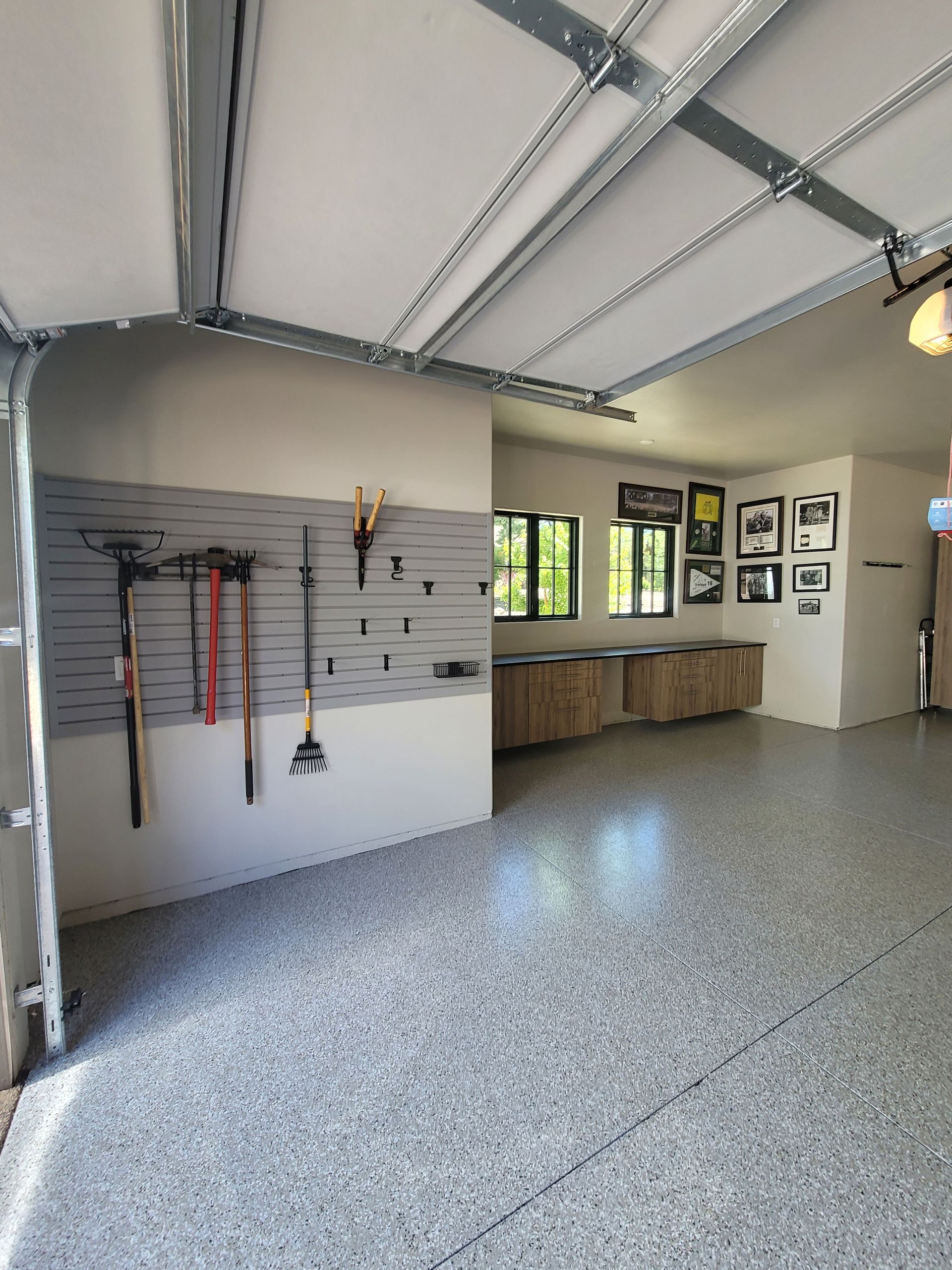 Spacious garage with speckled floor, wall-mounted tools, cabinets, and windows letting in natural light