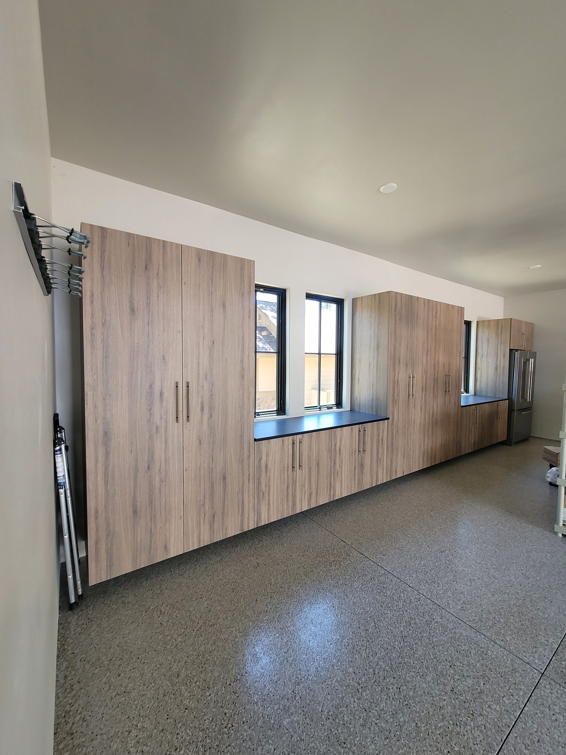 Long office wall with wood cabinets, windows, and speckled floor in a bright room