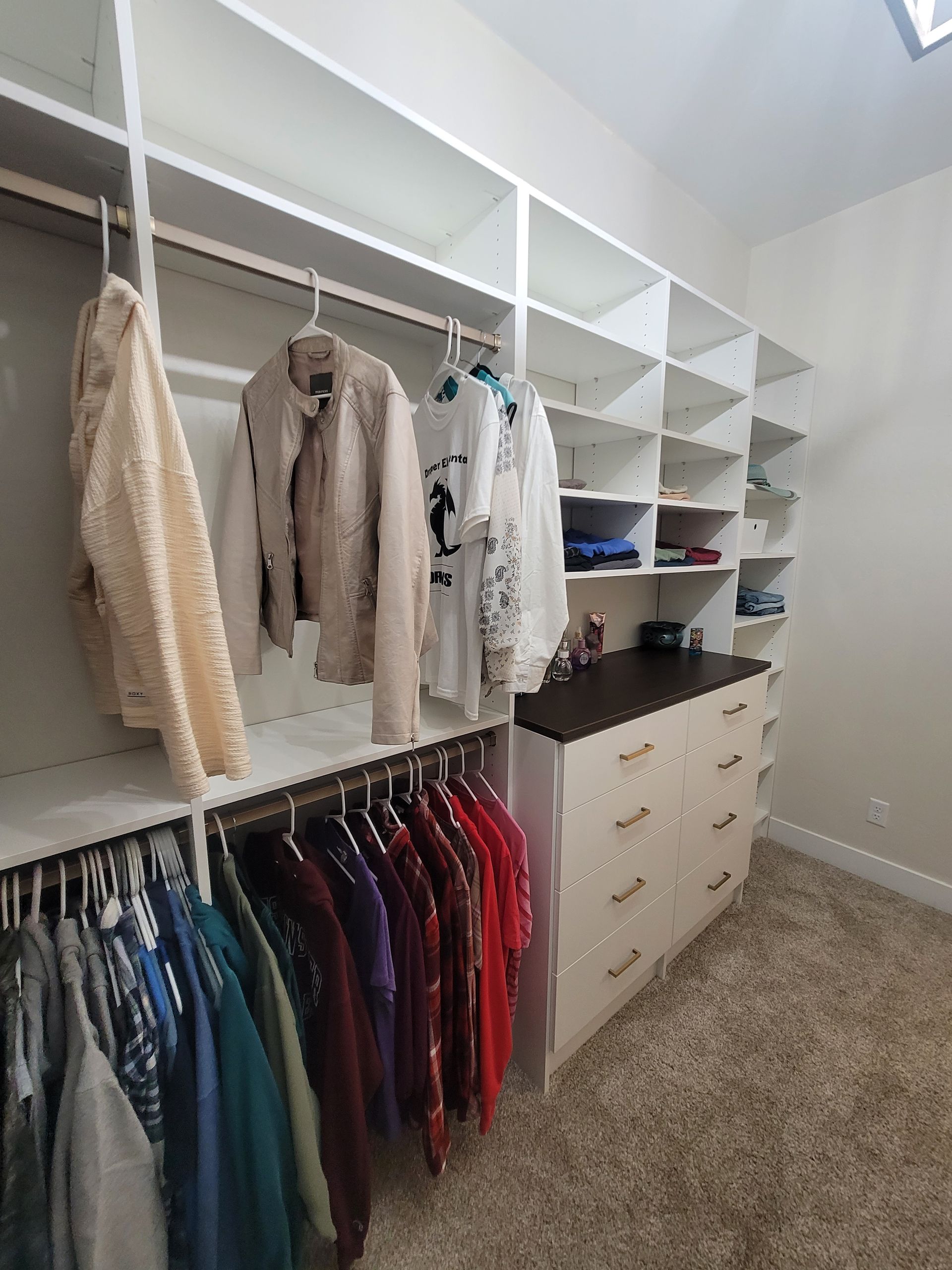 Walk-in closet with white shelving, hanging clothes, drawers, and carpeted floor