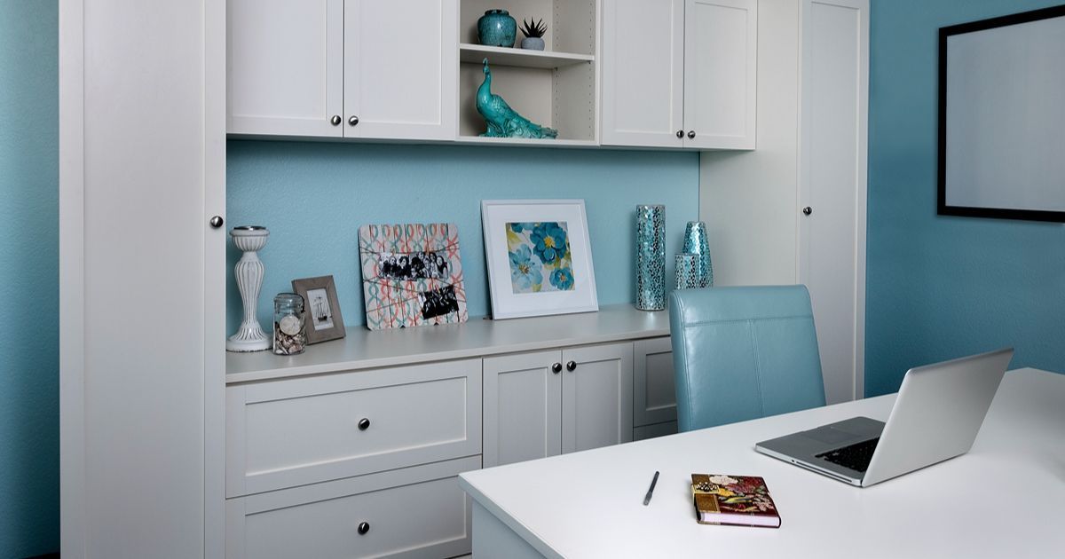 Bright home office with white desk, laptop, and light blue shelving against a blue wall.