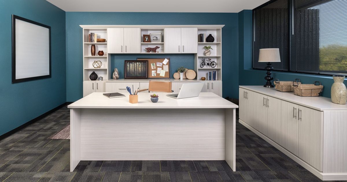 Modern home office with teal walls, white desk and shelving, window seat, and framed wall art