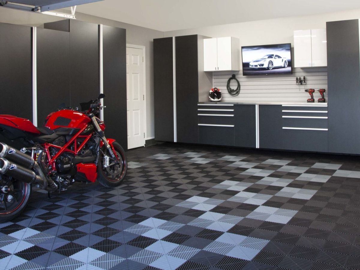 Motorcycle in a black-and-gray checkered garage with cabinets, tools, and a wall-mounted TV.