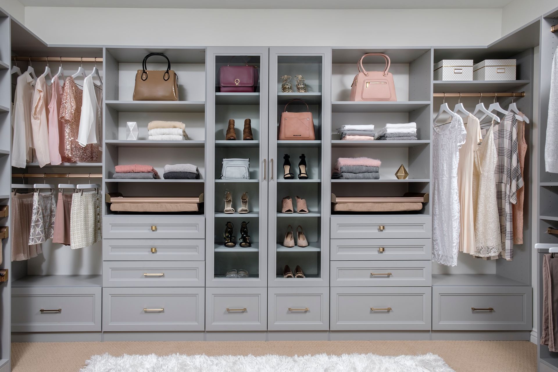 Gray walk-in closet with neatly organized clothing, including shirts, pants, and accessories. Neutral tones and a modern design are featured.