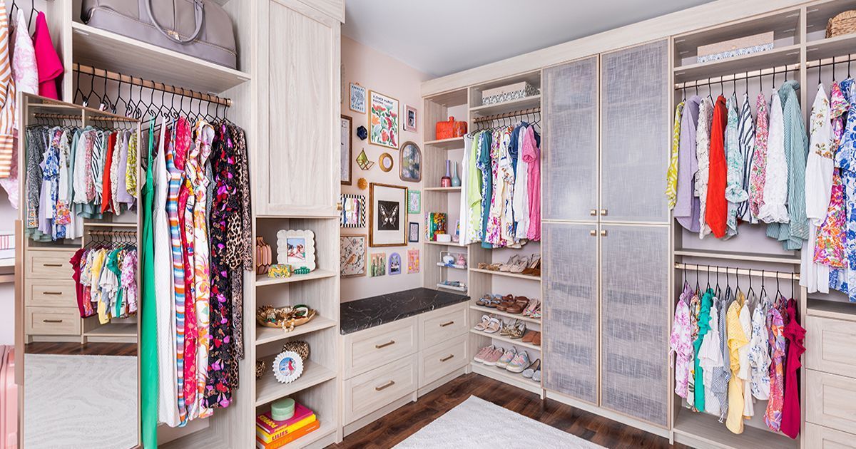 Walk-in closet with colorful clothing displayed on racks and shelves, neutral tones, and a sitting area.