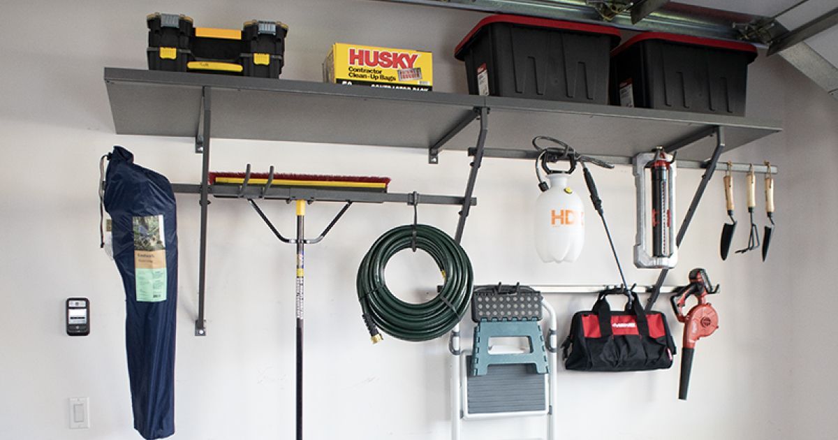 Garage wall with organized hanging tools, storage bins, hoses, and a blue apron on hooks.