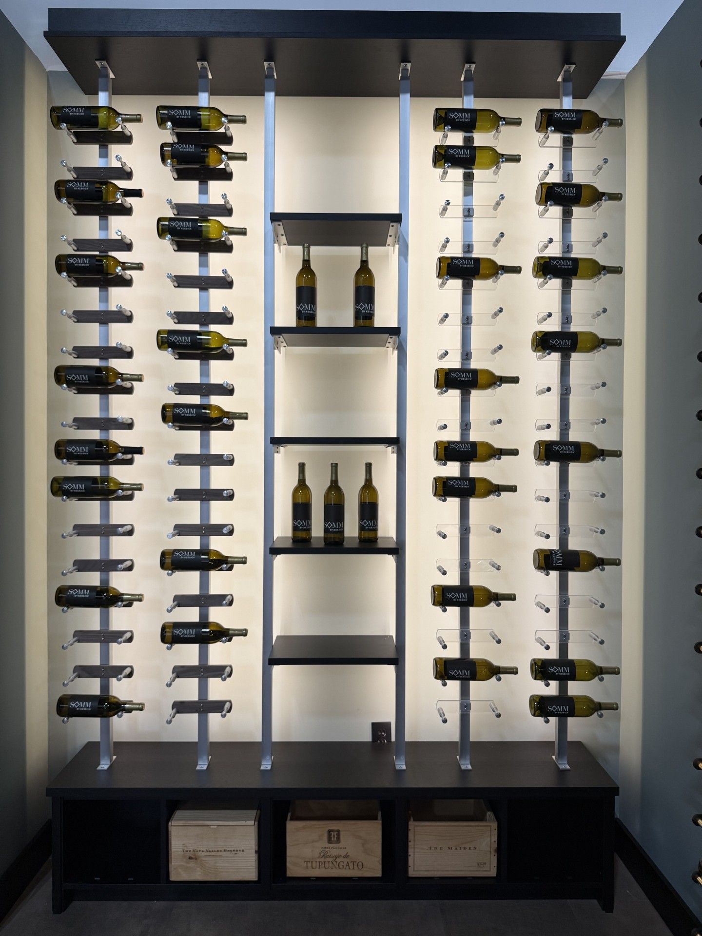 Wine bottles displayed on a wall-mounted rack with shelves and boxed storage below