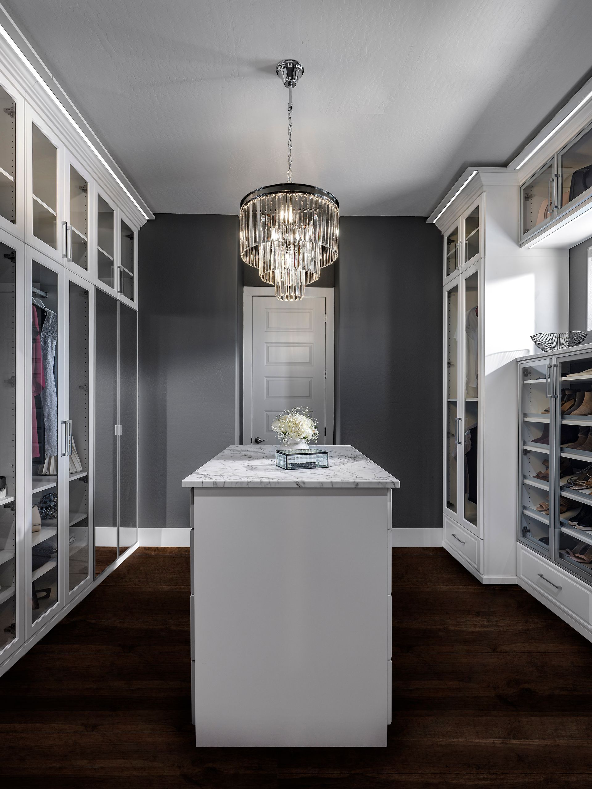 Modern walk-in closet with mirrored cabinets, gray walls, and a central island under a chandelier