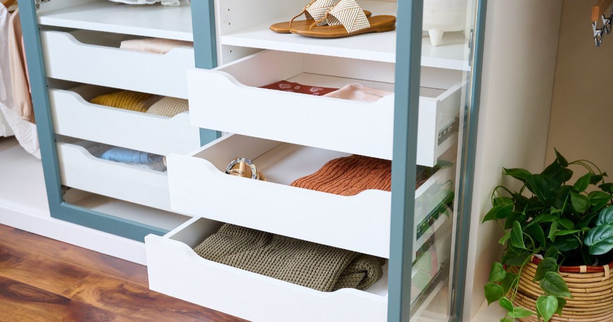 White drawer unit with folded clothes and baskets beside a potted plant on a wooden floor.