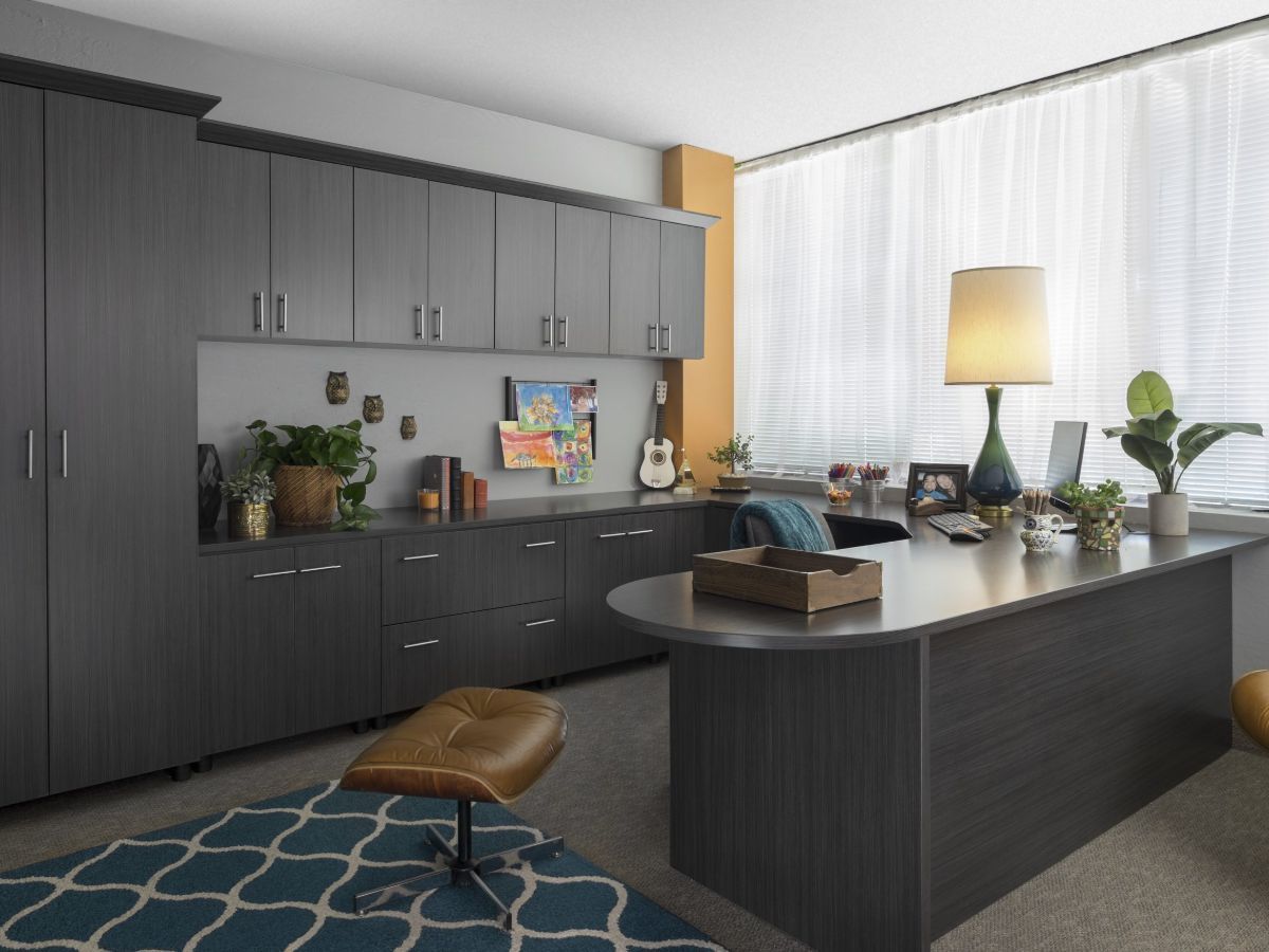 A home office with a desk , chair , lamp and cabinets.
