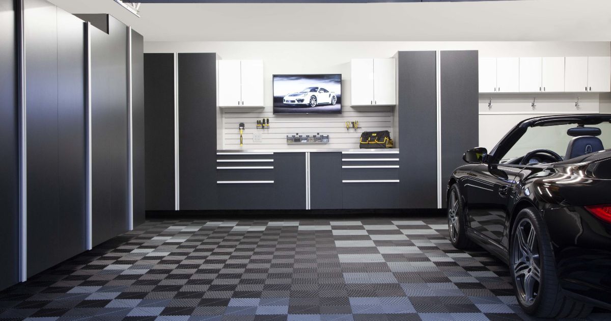 Modern garage with gray cabinets, checkered floor, wall TV, and a black car on the right