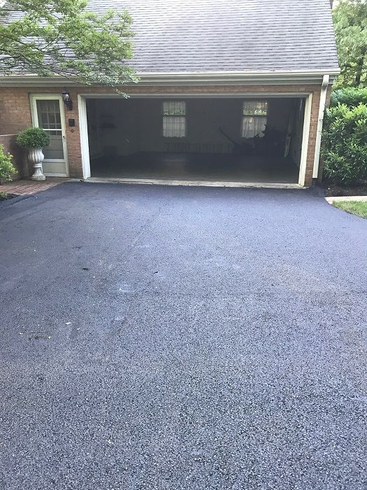 Newly paved asphalt driveway in front of a garage with an open door.